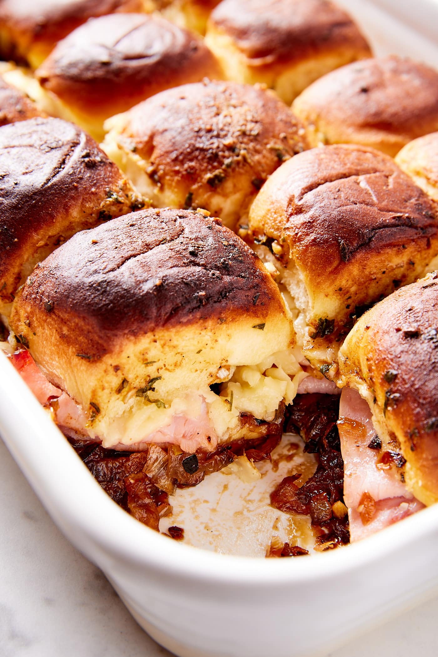 White baking dish filled with slider sandwiches with ham and cheese and onion jam mixture on the inside.