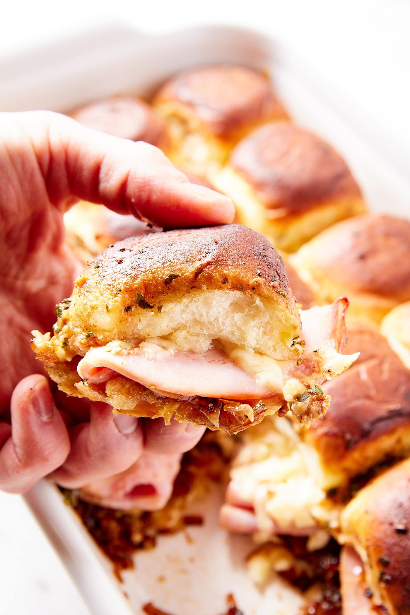 Hand holding ham and onion jam slider with ham and cheese showing in the middle of the sandwich.