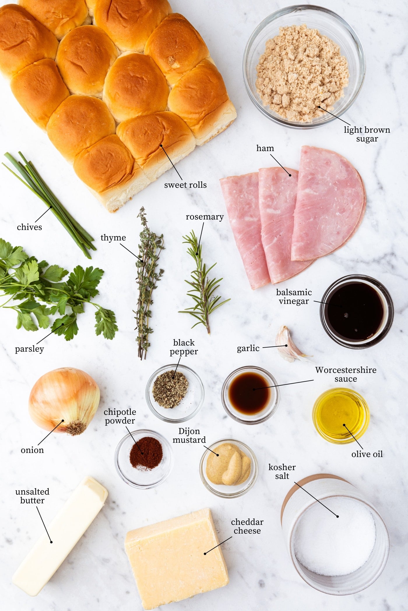 White marble surface filled with all ingredients needed to make ham and onion jam sliders including rolls, ham, herbs, spices, and more.