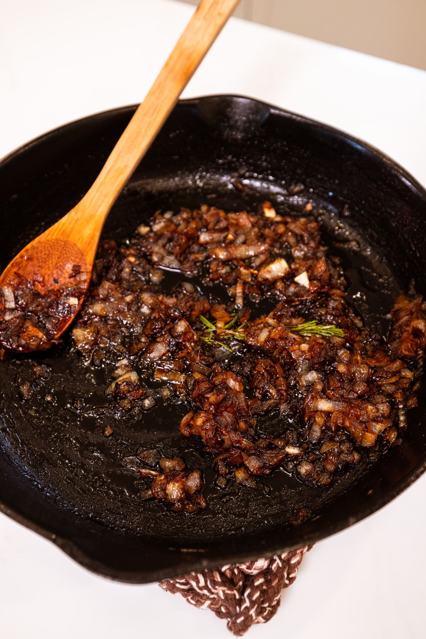 Black cast iron skillet filled with candied onions forming a jam with wooden spoon resting on side.
