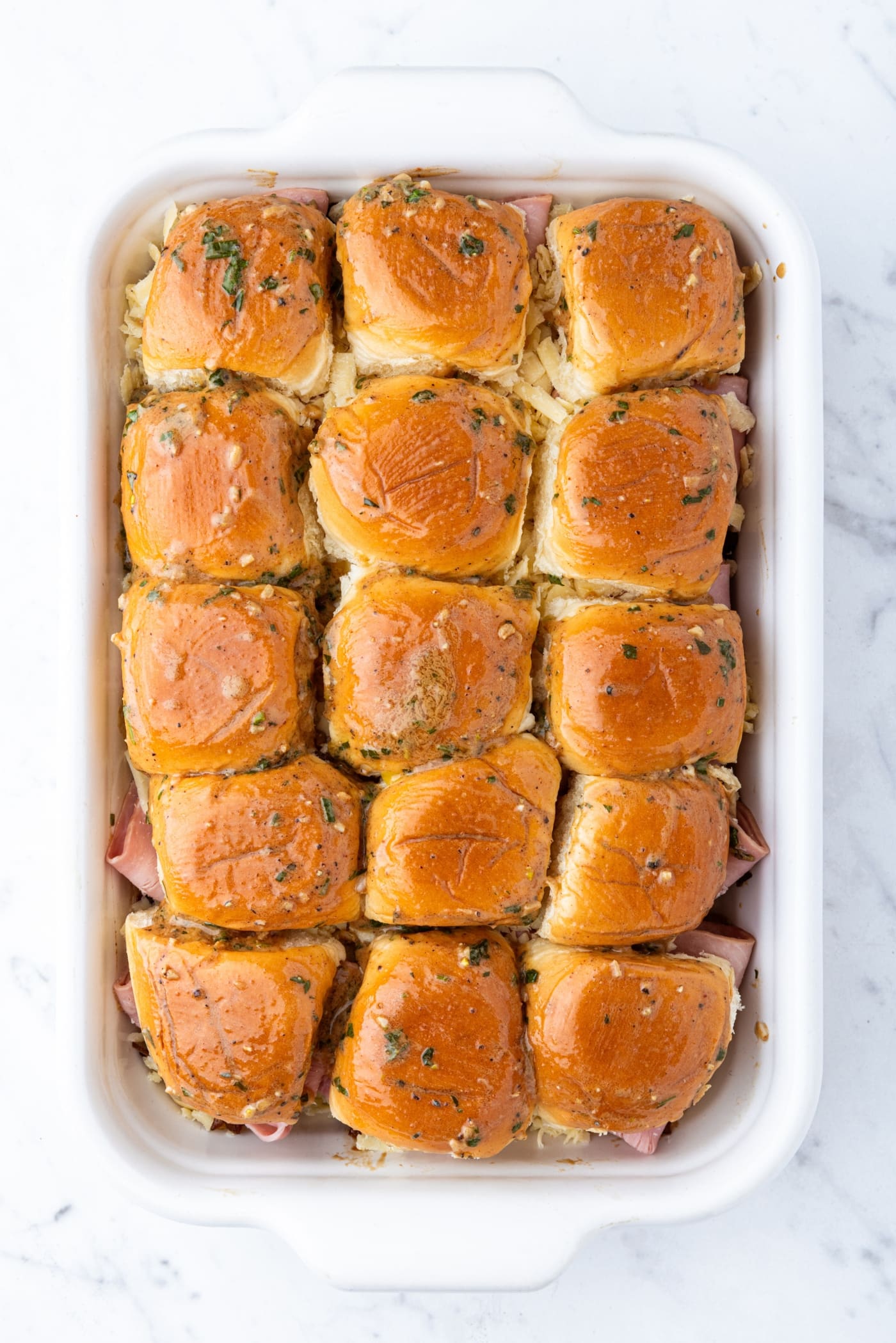 Ham and onion jam sliders sitting in white baking dish sitting on marble surface right before being baked.