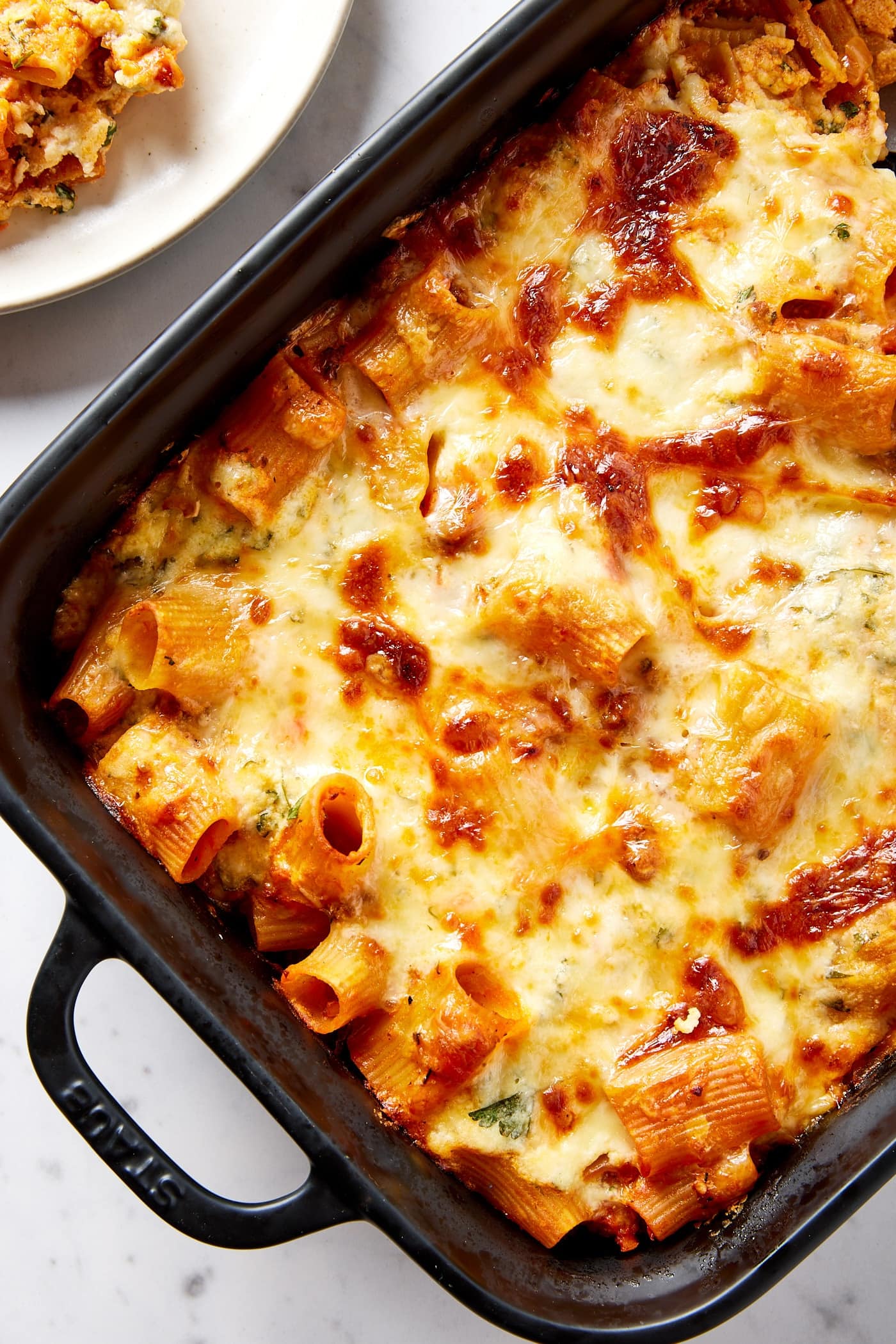 Black baking pan filled with baked lasagna casserole with browned top and plate with serving to the side.