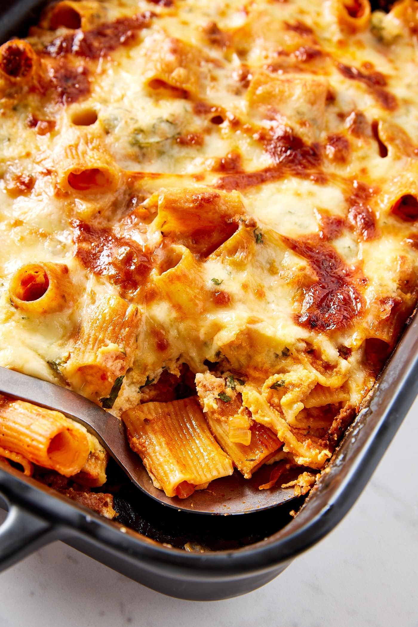 Rectangular baking dish filled with baked lasagna casserole with spoon scooping out a serving.