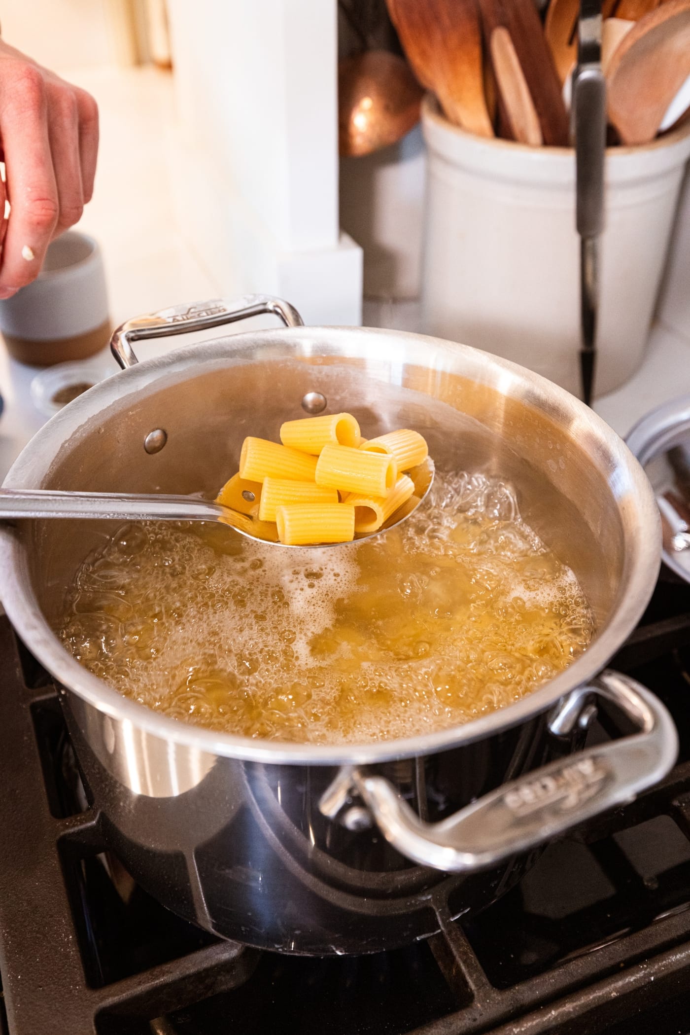 Spoon filled with cooked pasta with rest of pasta still in water in stockpot on the stove.