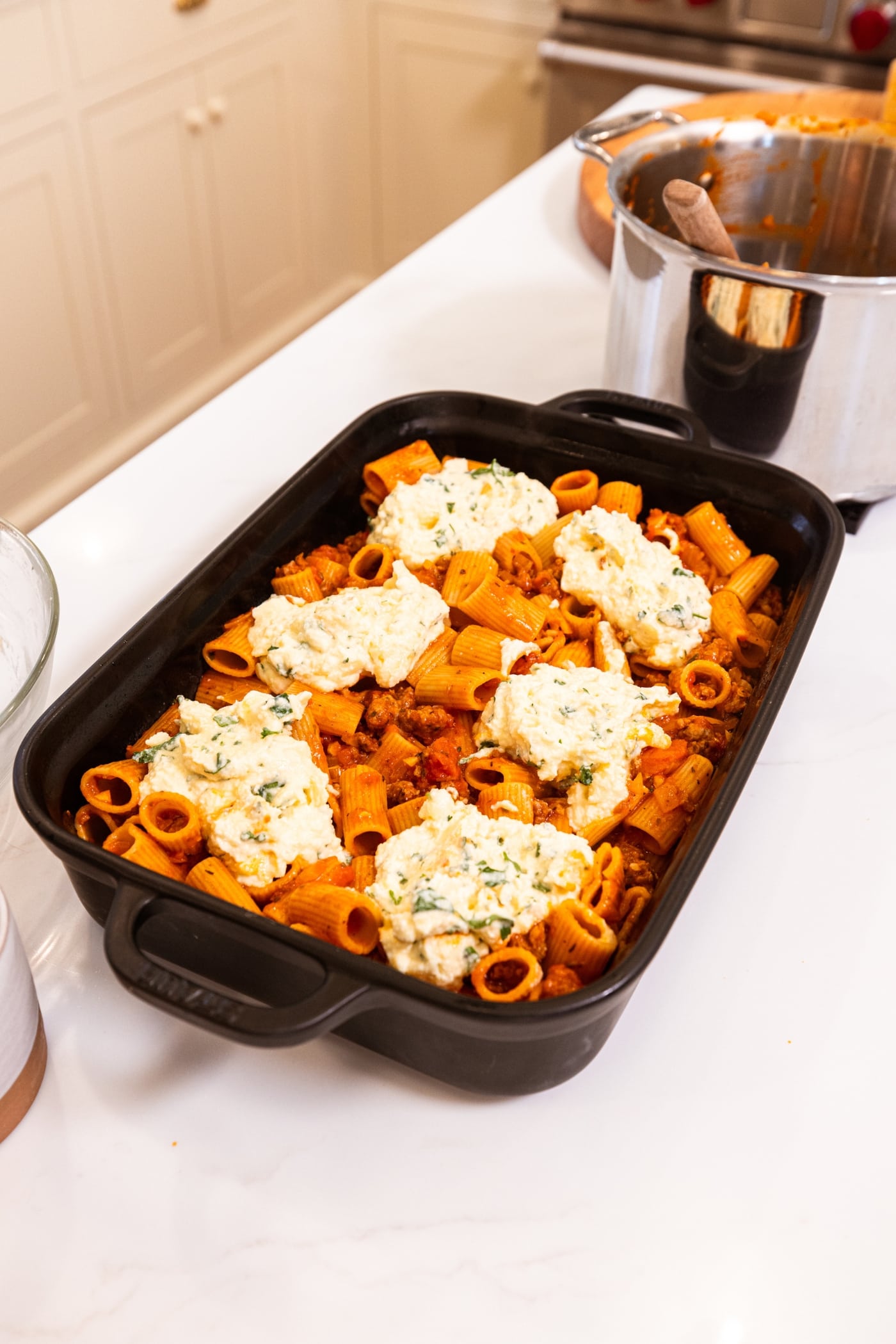 Black rectangular baking dish filled with uncooked mixture of lasagna casserole with pockets of ricotta mixture.