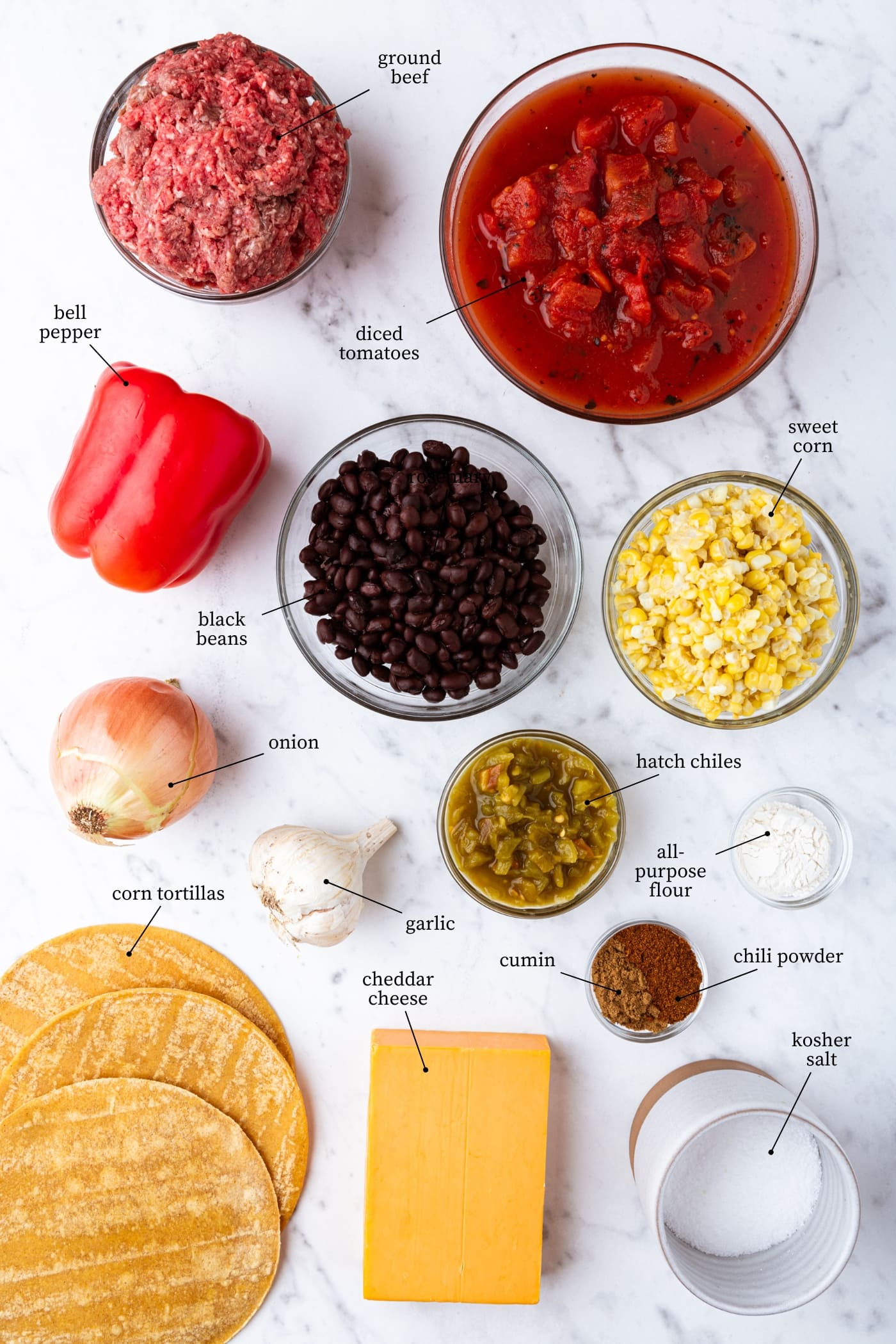 White marble surface filled with all ingredients for loaded taco squares casserole including beans, raw beef, corn tacos, corn, and more.