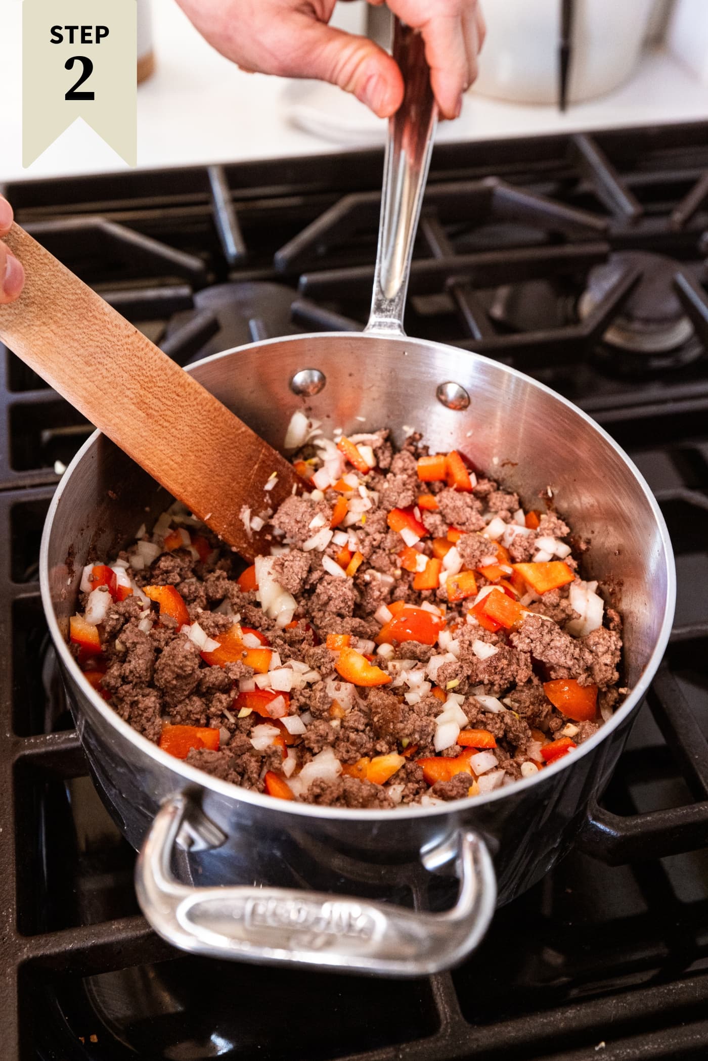 Mixture of browned beef with onion and red bell pepper all cooking on the stovetop.