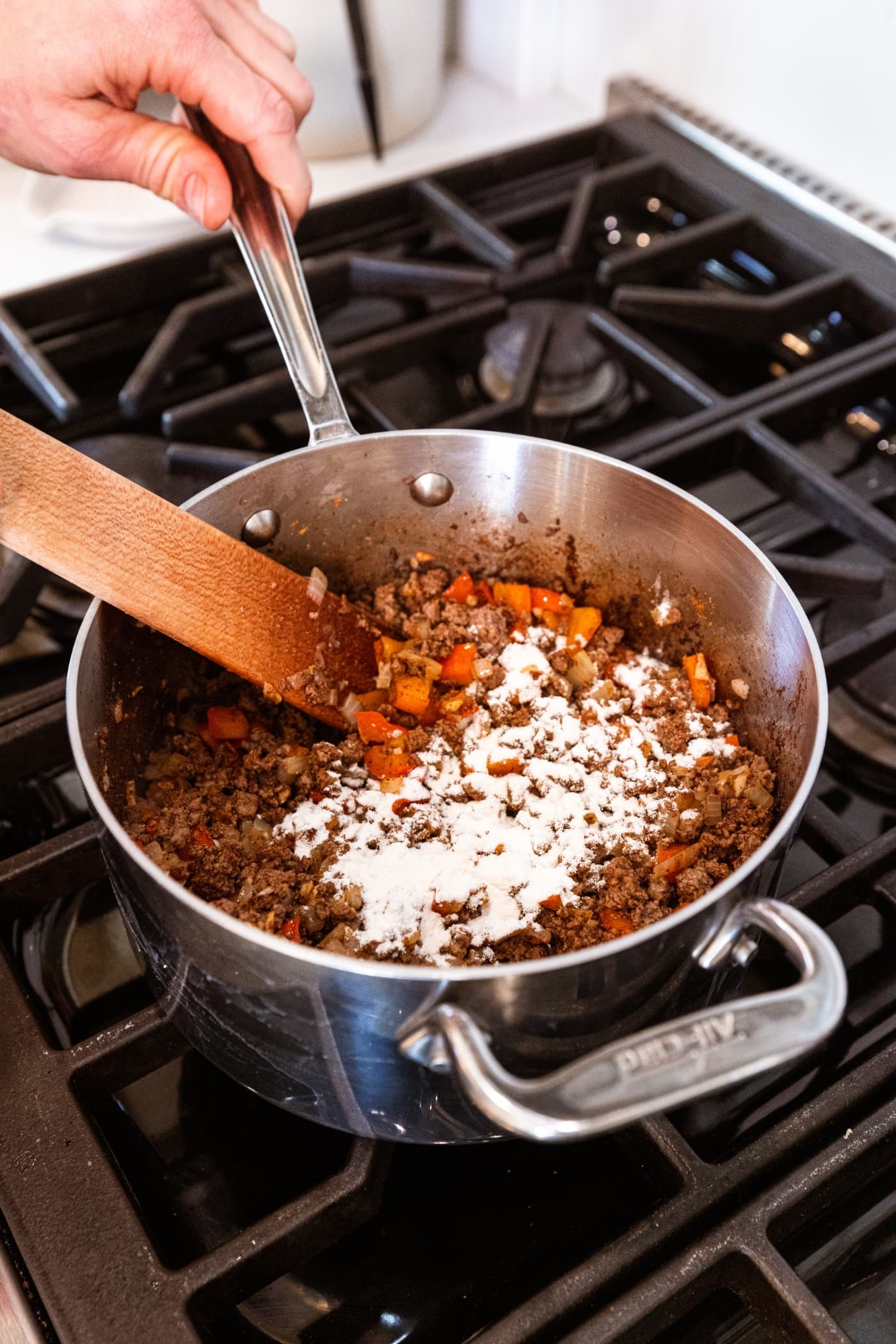 Sprinkled flour all over the top of ground beef and bell pepper mixture cooking on the stovetop.