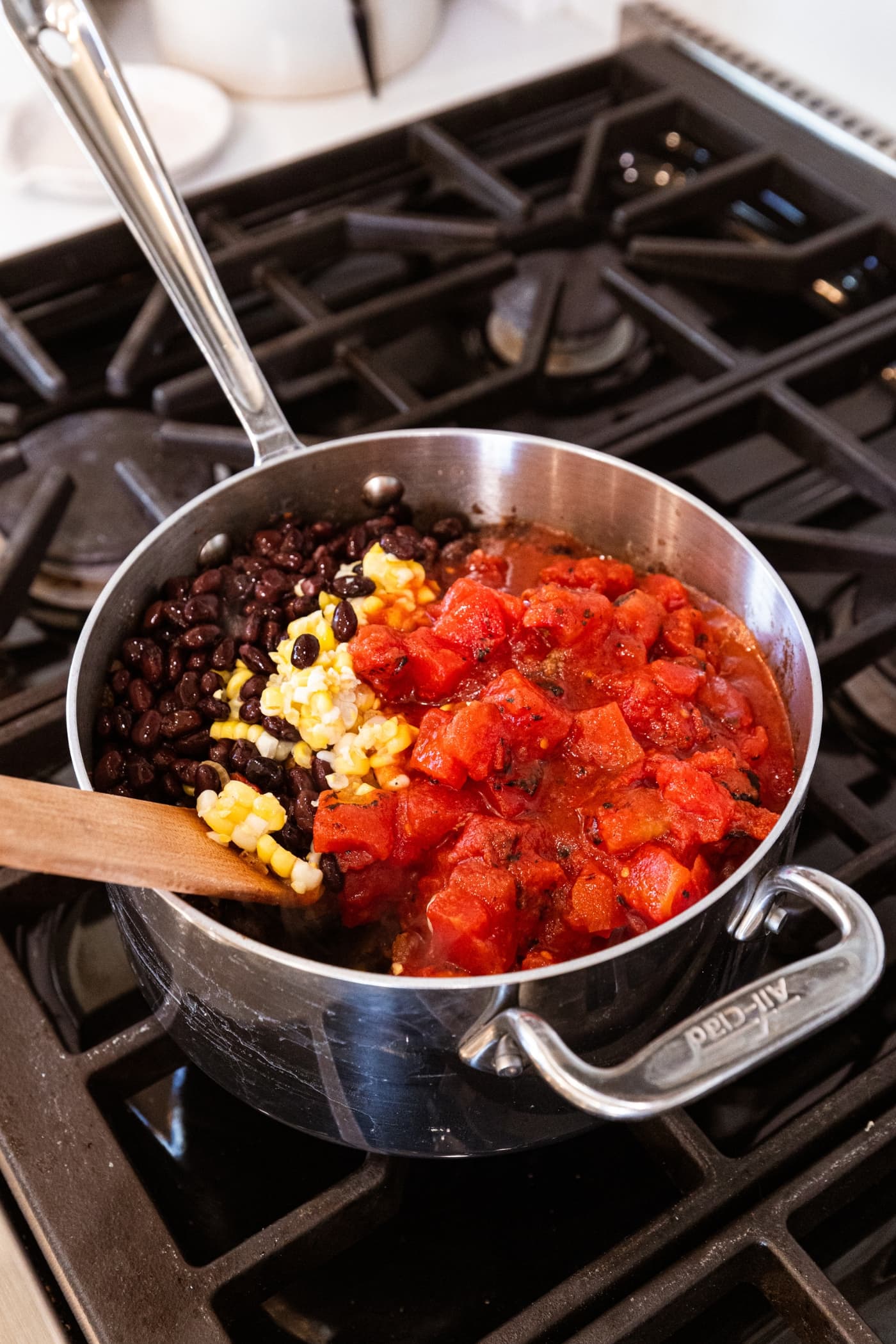 Mixture of black beans, sweet corn, and diced tomatoes in a metal saucepan on the stovetop.