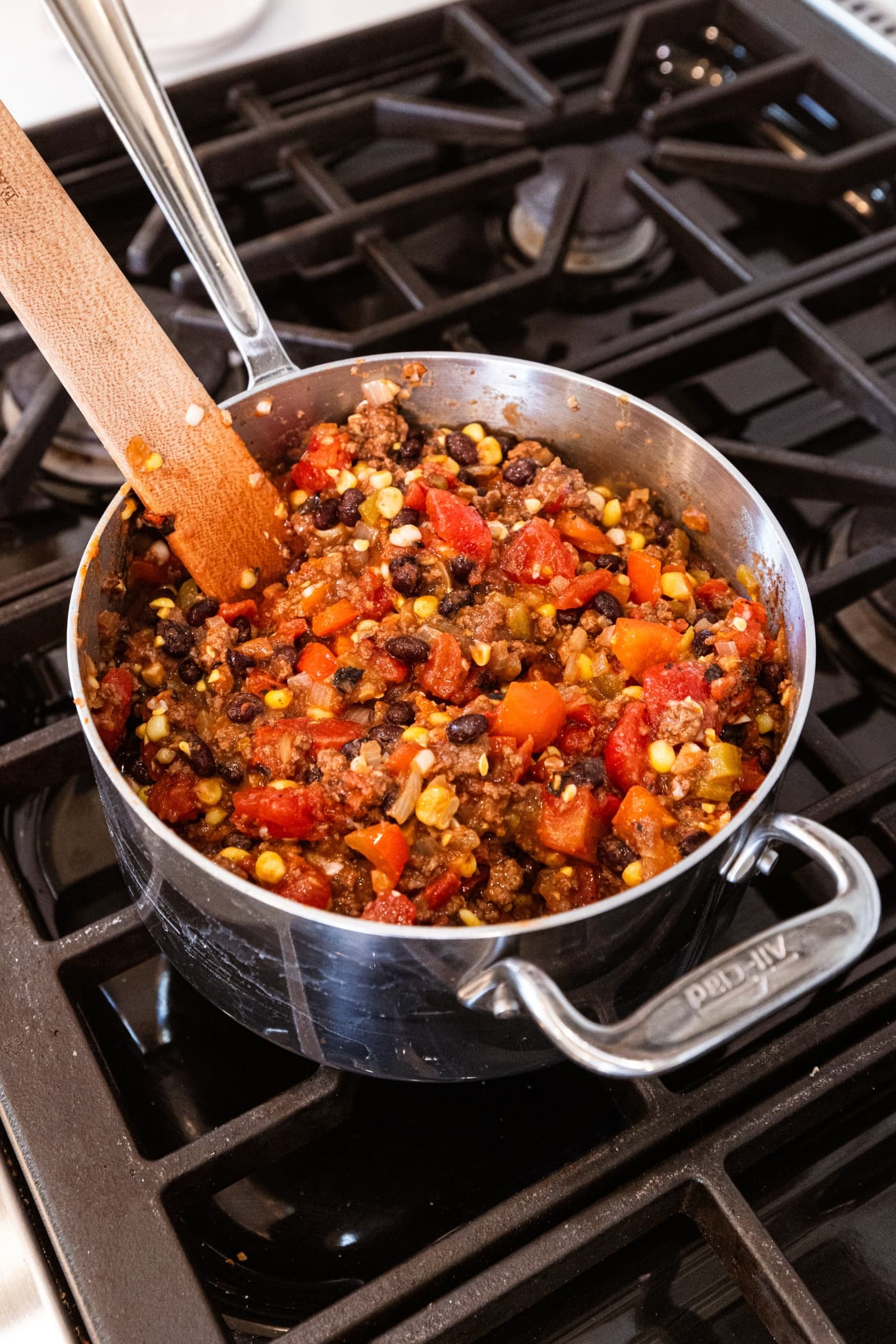 Mixture of ground beef, sweet corn, black beans, and tomatoes all mixed together in a saucepan.