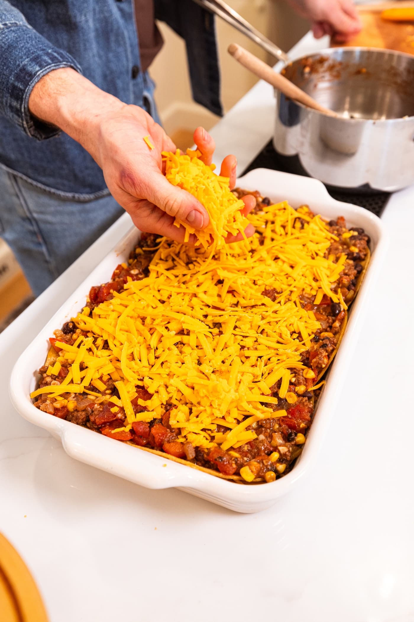Hand spreading shredded cheese on top of a ground beef mixture in a baking dish.