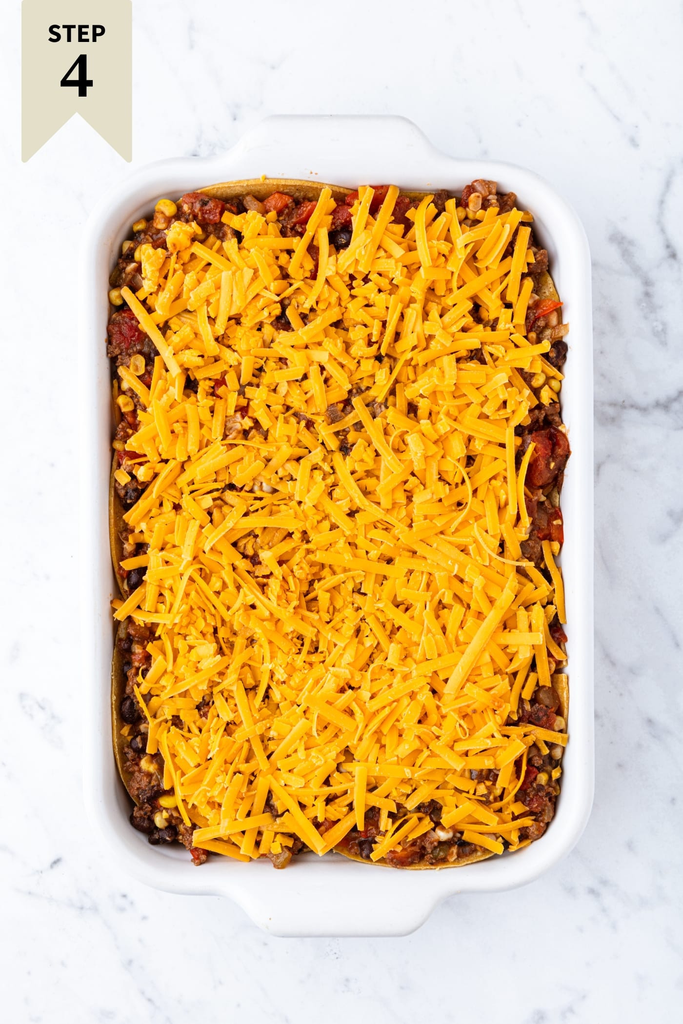 White marble surface filled with rectangular baking dish with shredded cheese spread on top before being baked.