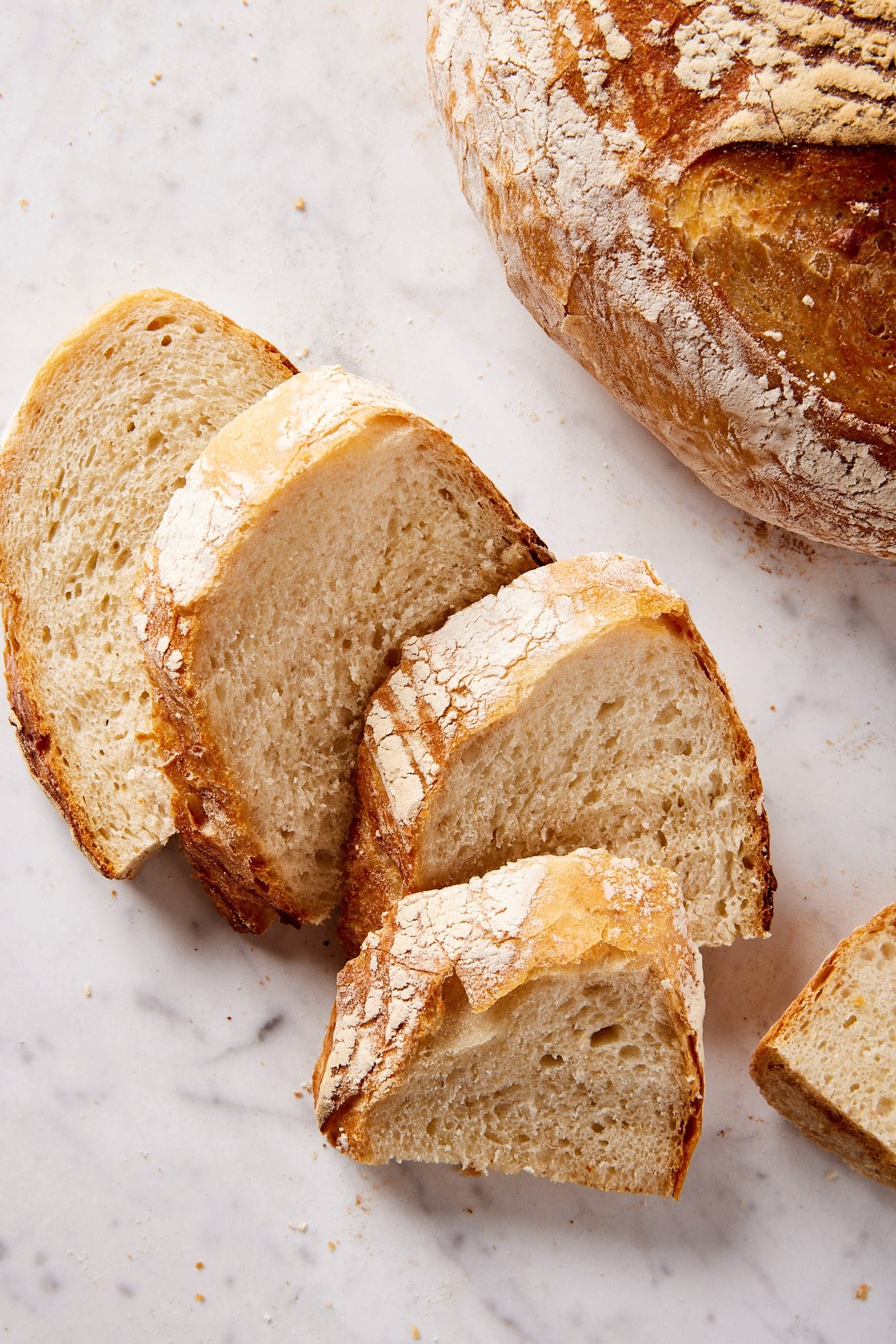 Slices of overnight sourdough bread resting on marble surface with rest of loaf in the background.