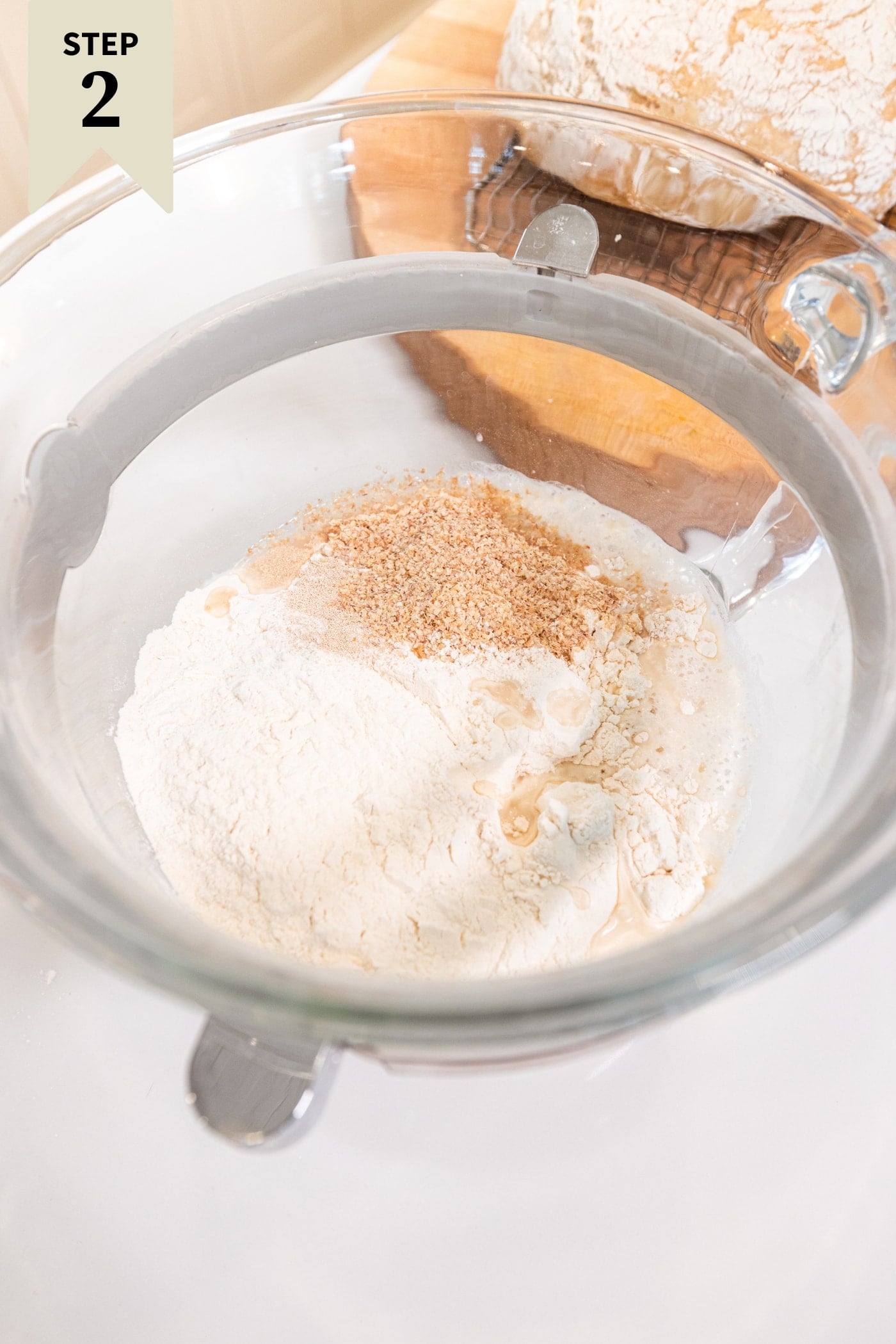 Glass mixing bowl filled with flour, poolish, wheat germ, and yeast before being mixed together on stand mixer.