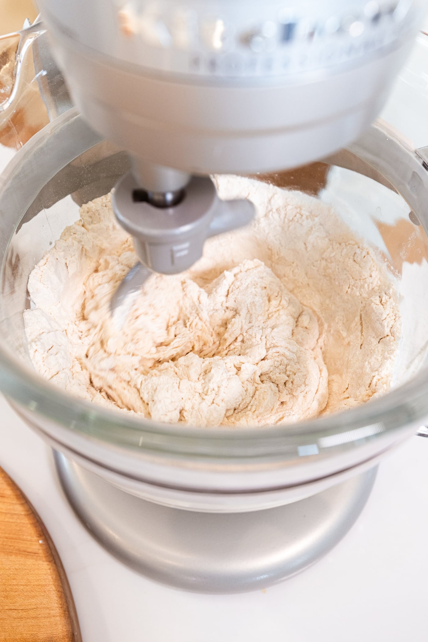 Glass mixing bowl on stand mixer with dough hook mixing everything together for an overnight sourdough bread.