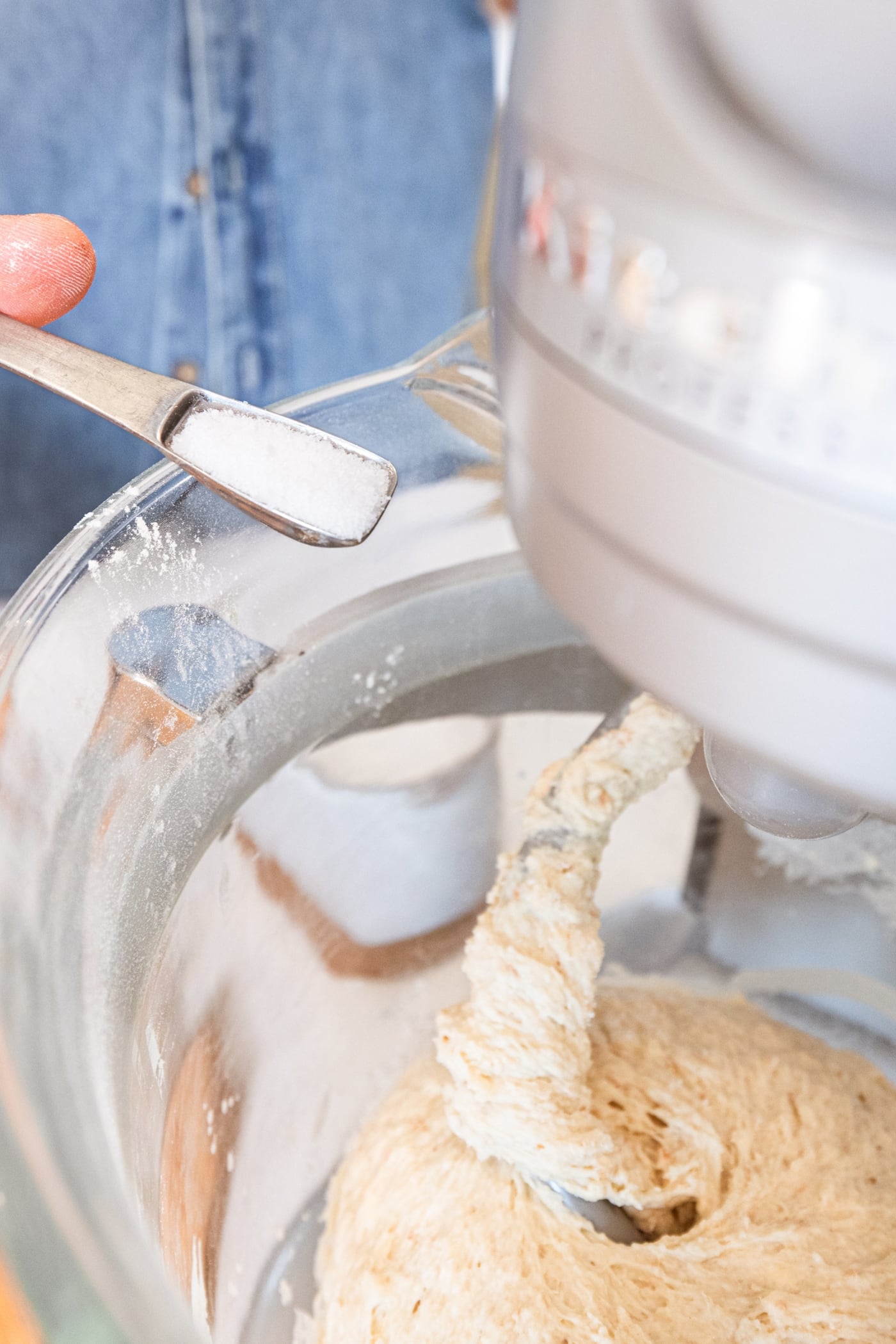 Small teaspoon adding kosher salt to a glass mixing bowl on a stand mixer.