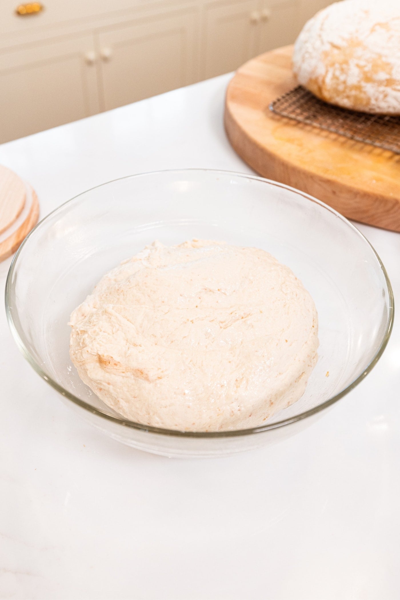 Glass bowl filled with dough before having risen all on white surface.