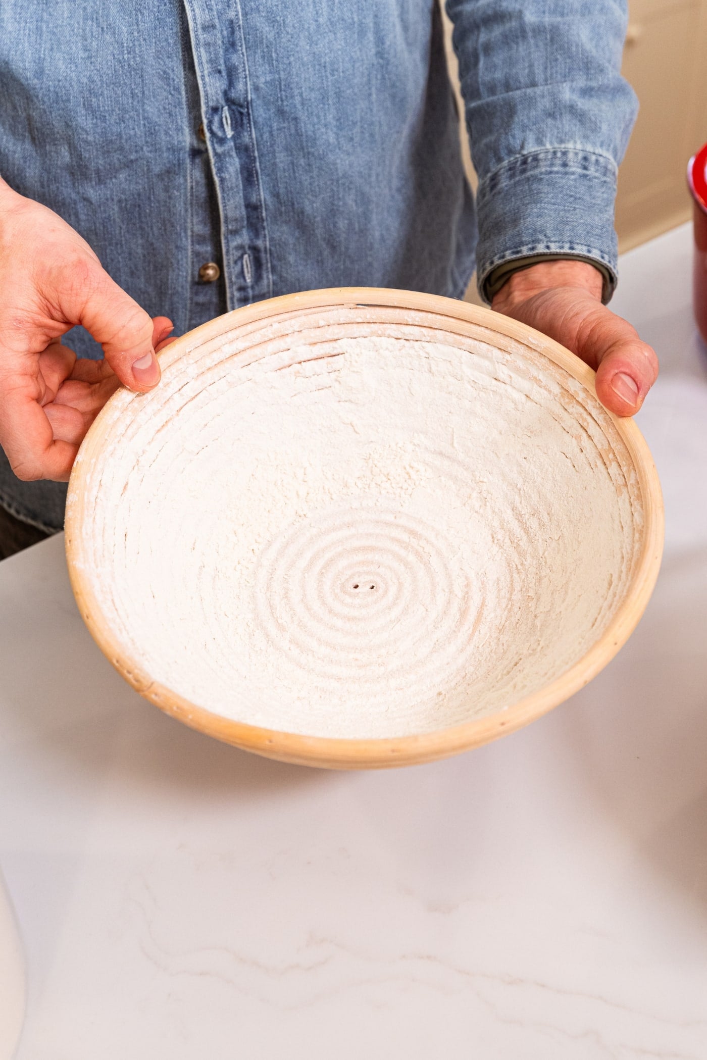 Hand placing flour in a round bowl made for bread to rise in.