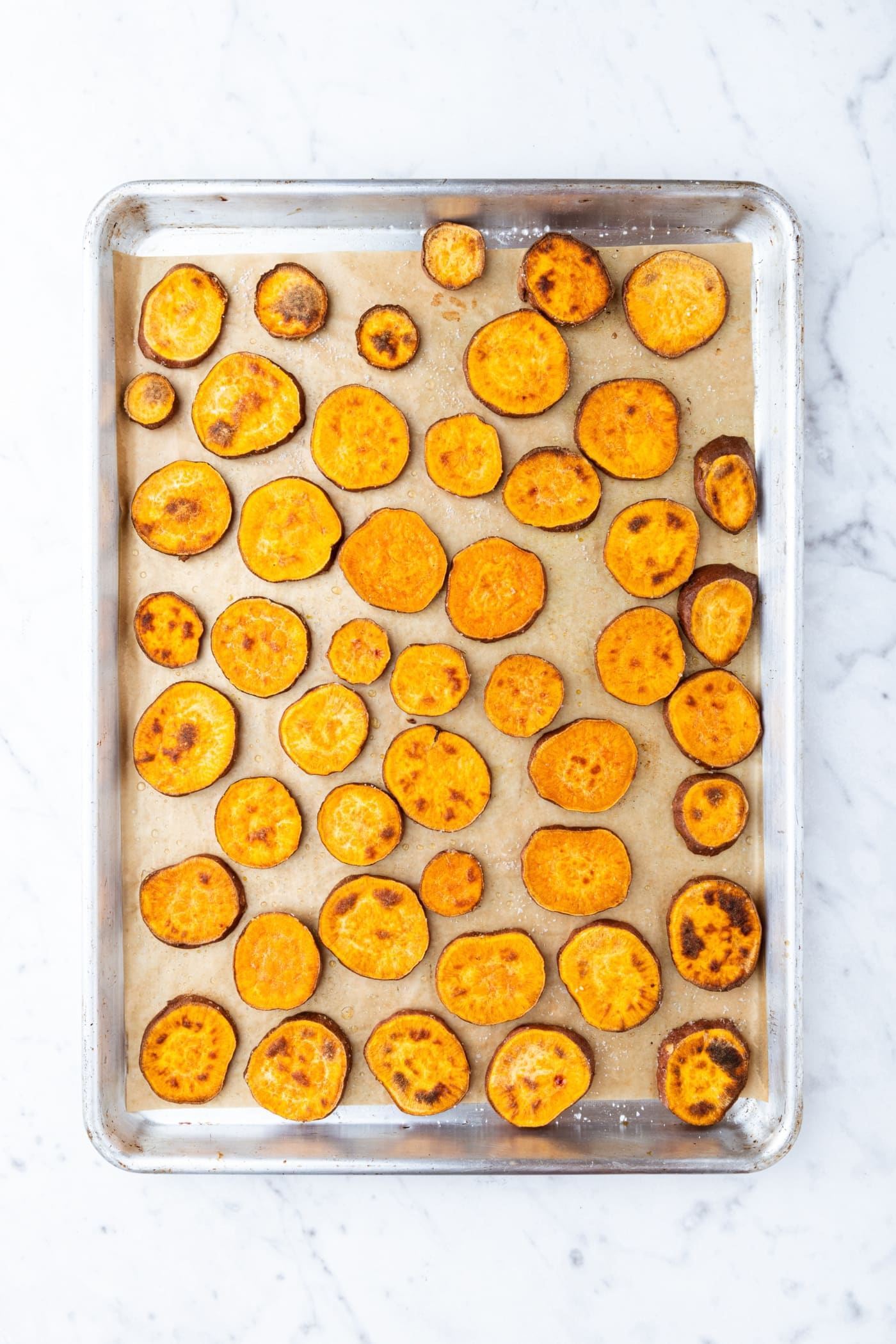 Sweet potato slices on a parchment-lined baking sheet right after coming out of the oven.