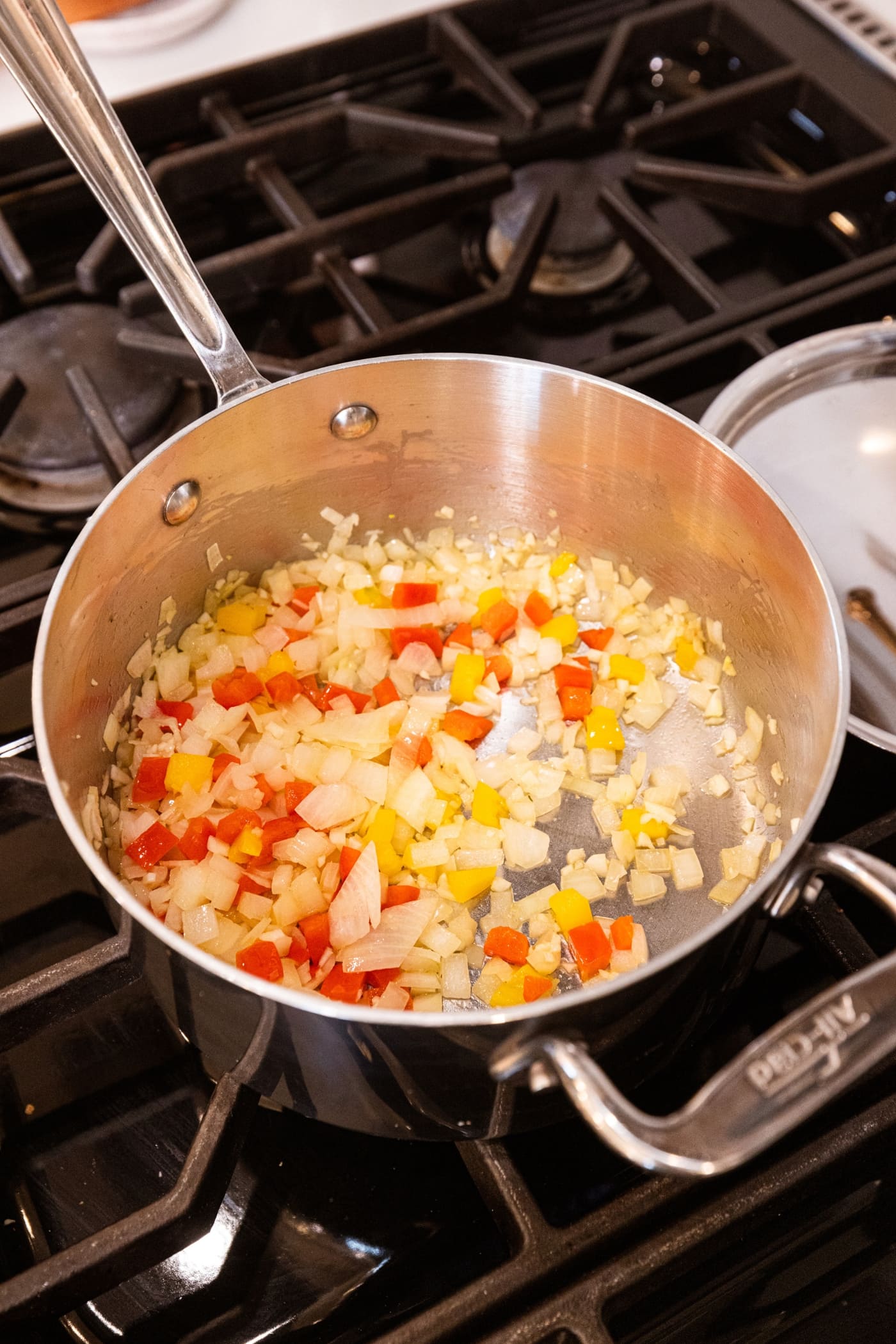 Metal pan filled with browned pieces of diced onion and bell peppers all on stovetop.
