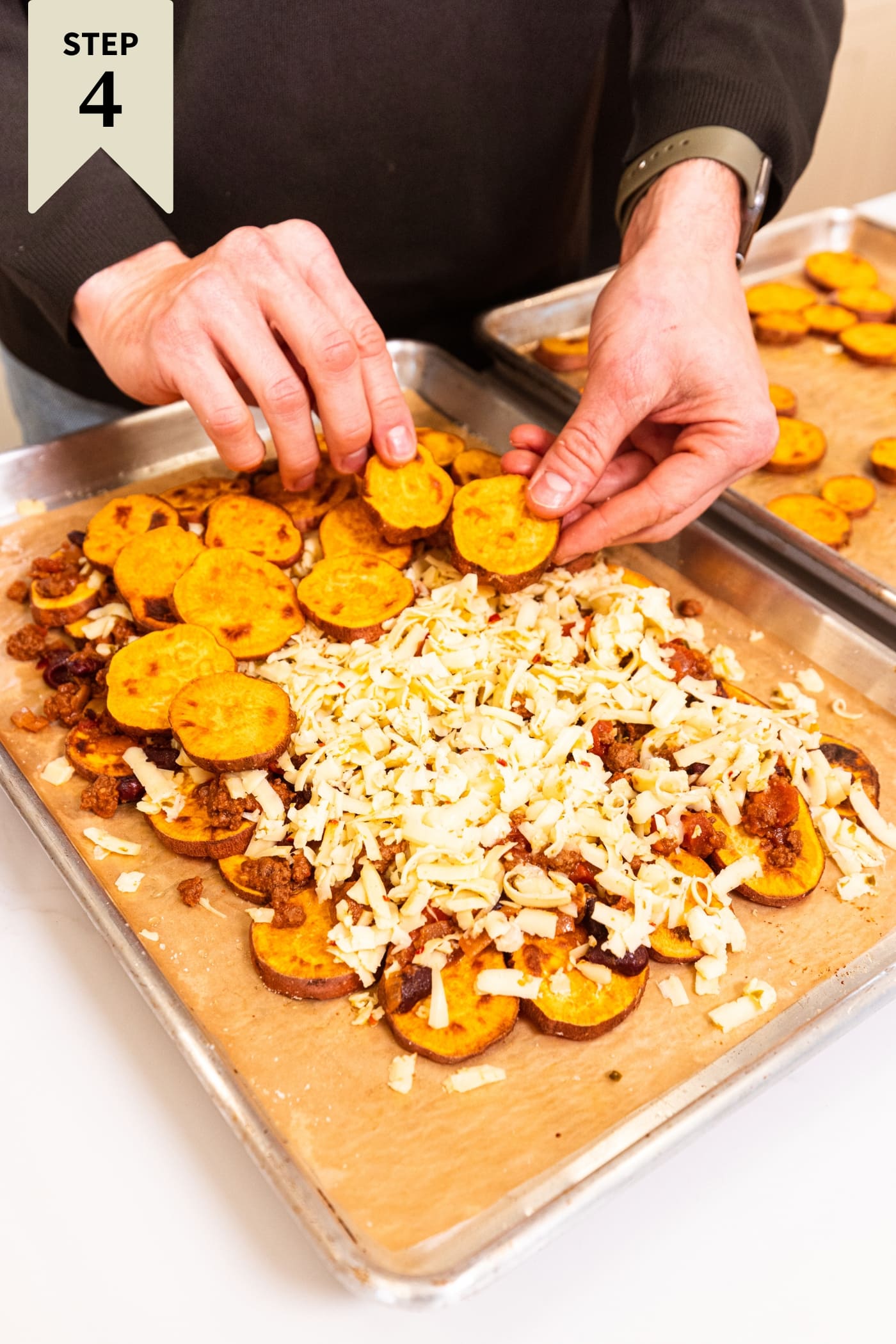 Hand assembling slices of roasted sweet potato on top of previous layers of sweet potato, chili, and cheese.
