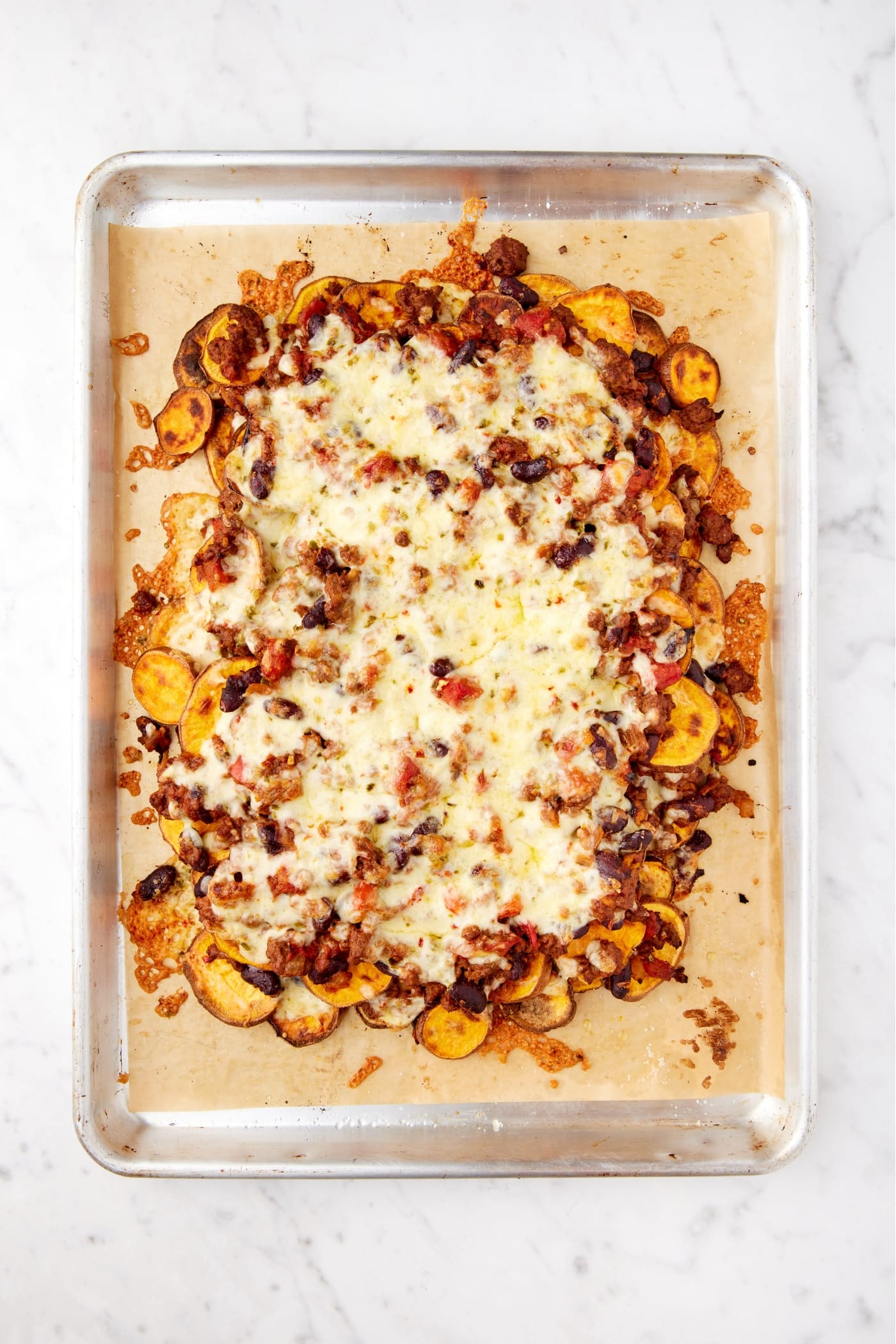 Sheet pan with layers of sweet potato chili nachos with melted cheese on top right after coming out of the oven.