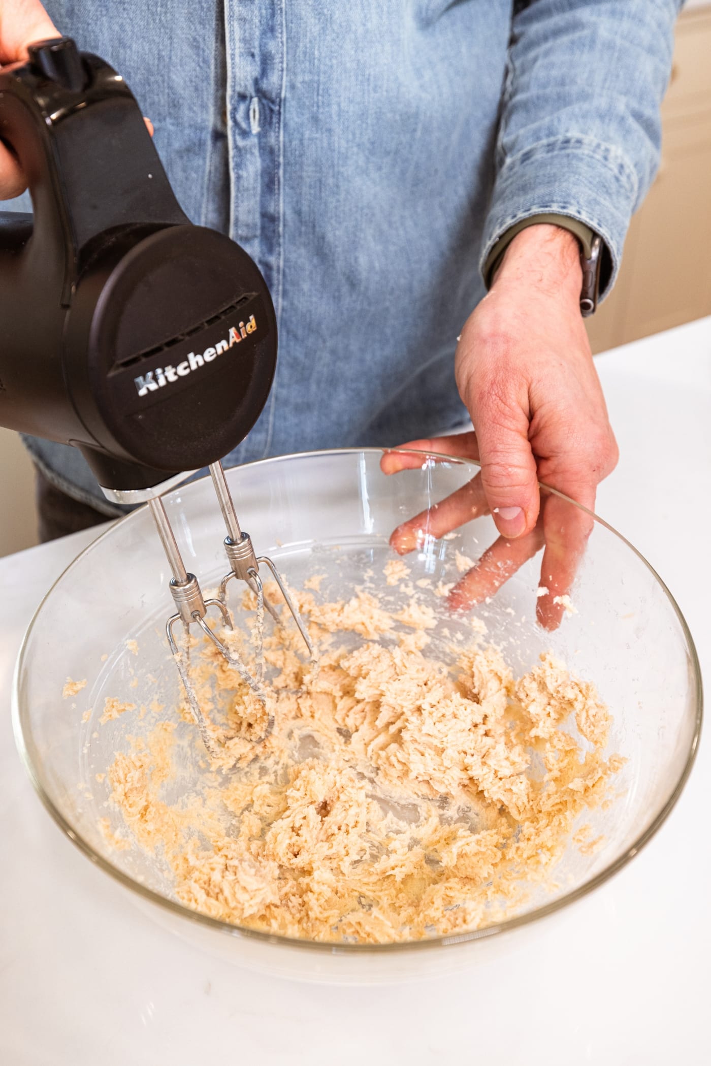 Hand mixer mixing together butter and sugar into a creamy mixture on white surface.