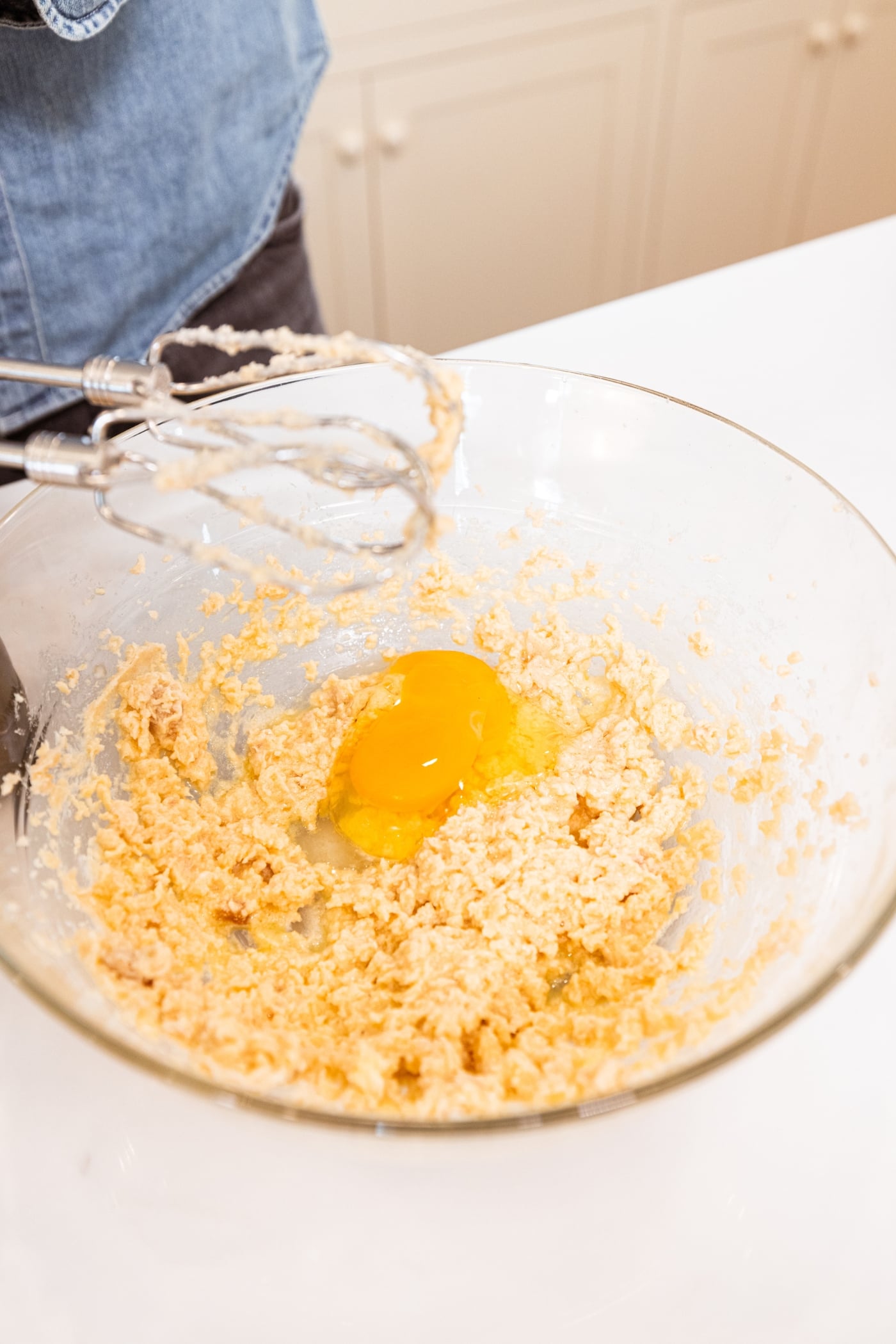 Eggs being added to a creamed butter and sugar mixture in a glass bowl.