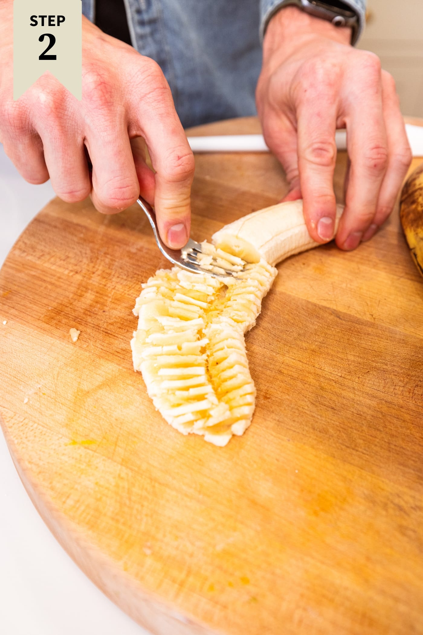 Hand using fork to mash banana on a wooden cutting board for banana bread.