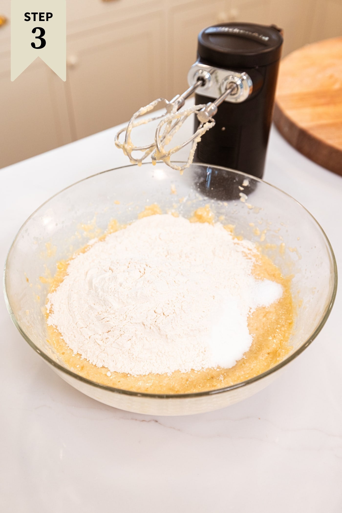Pile of flour and other dry ingredients on top of creamed sugar mixture in glass bowl for banana bread.