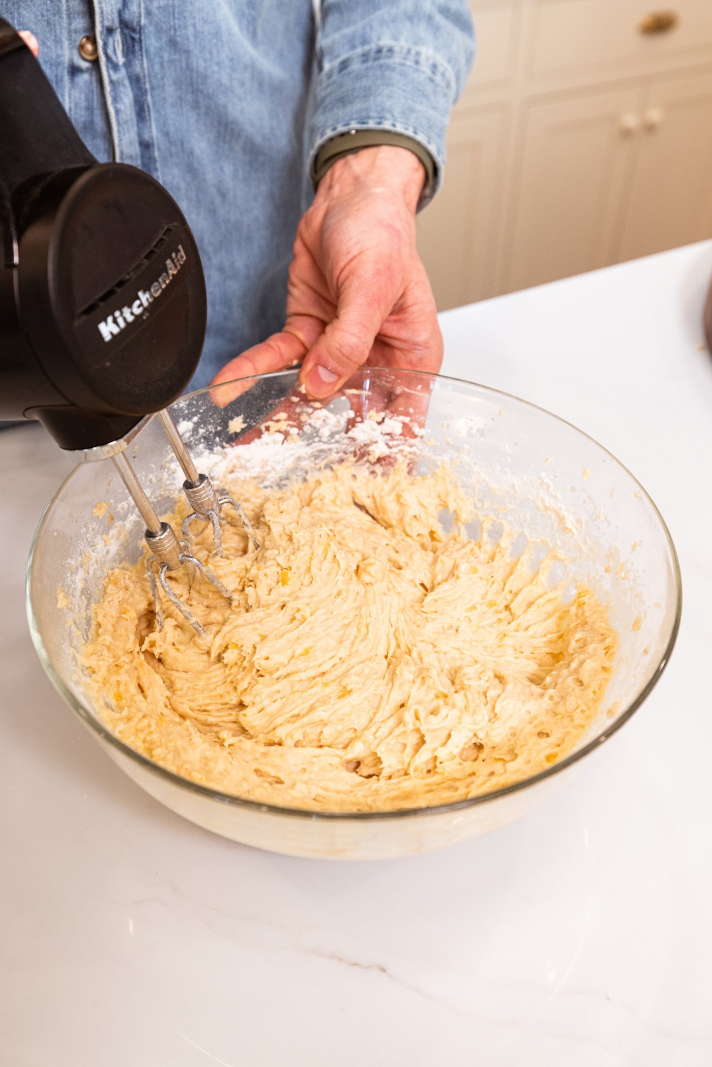 Hand mixer mixing together a batter for chocolate chip banana bread in glass bowl.