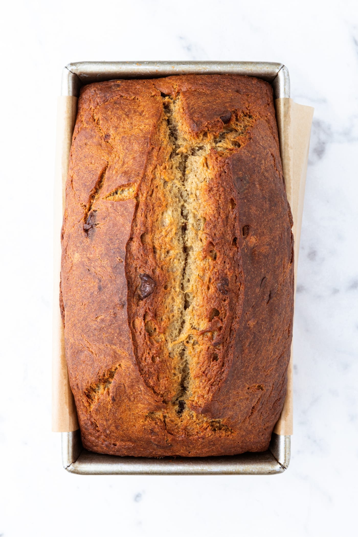 Baked and golden brown loaf of banana bread on marble surface right after coming out of the oven.