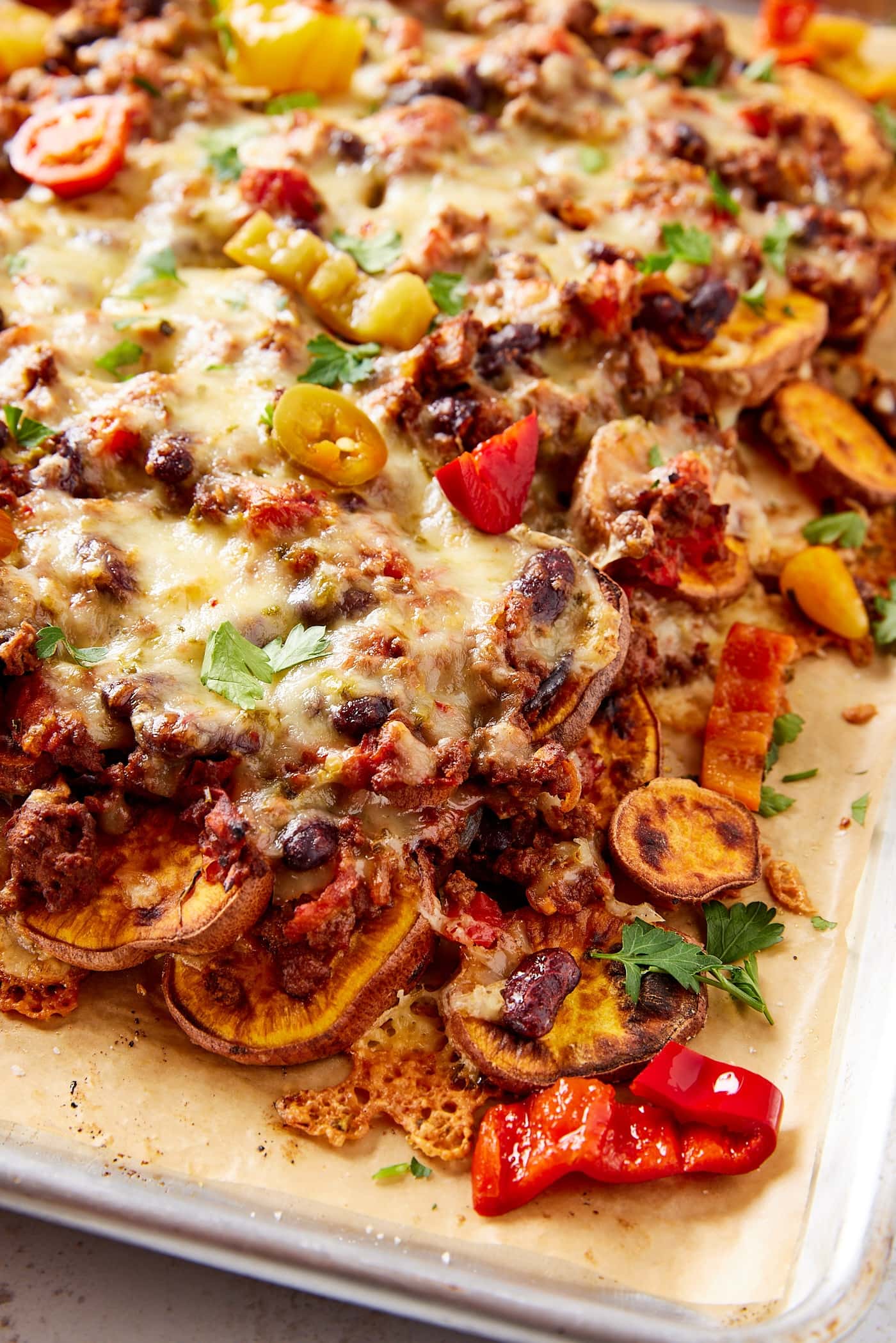 Sheet pan filled with layers of sweet potato with thick chili and melted cheese on top along with pickled peppers.