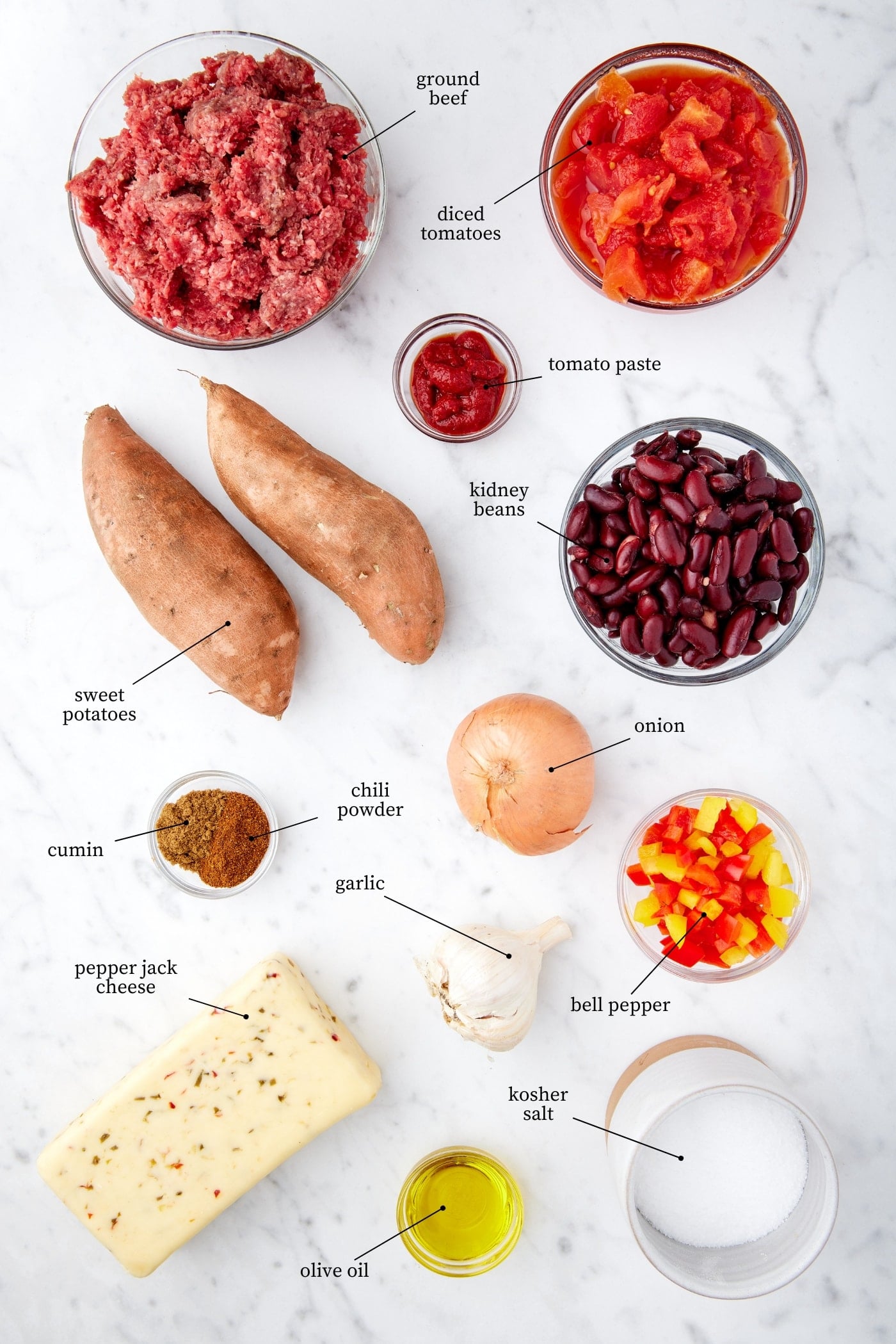 White marble surface filled with all ingredients needed to make sweet potato chili nachos including beef, tomatoes, bell peppers, cheese, sweet potatoes, and more.