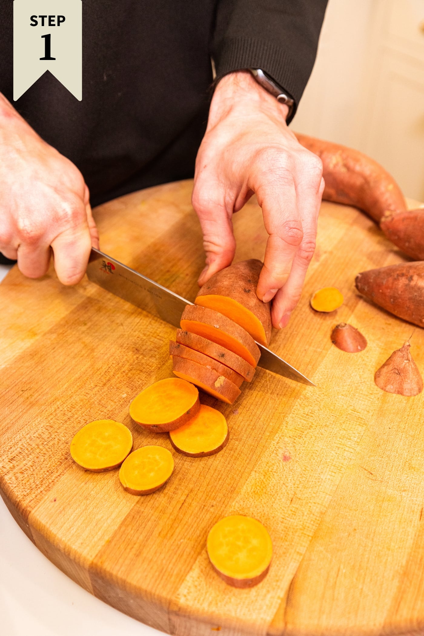 Hand slicing sweet potato into this slices on a wooden cutting board.