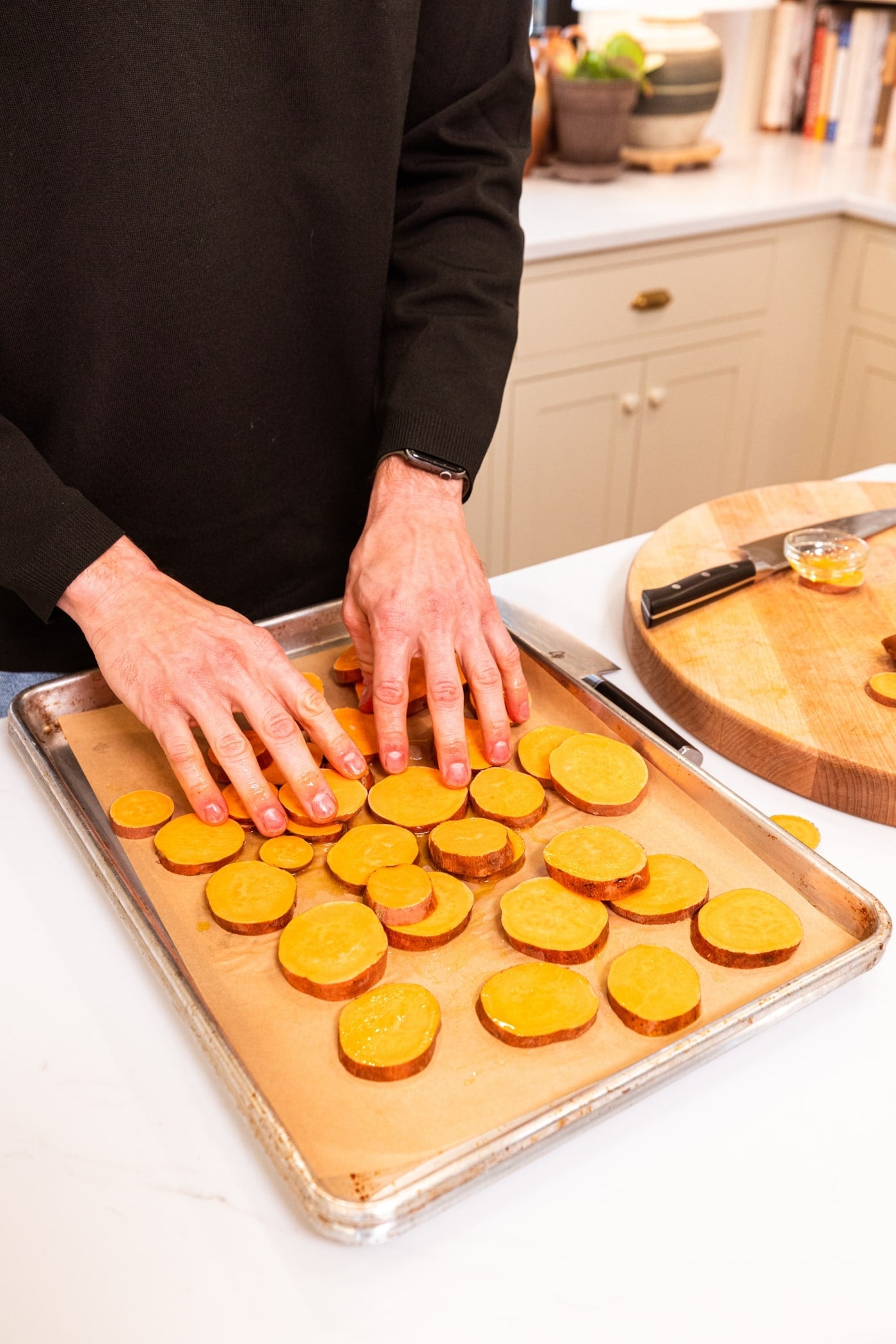 Hands arranging slices of sweet potato on a parchment-lined baking sheet.