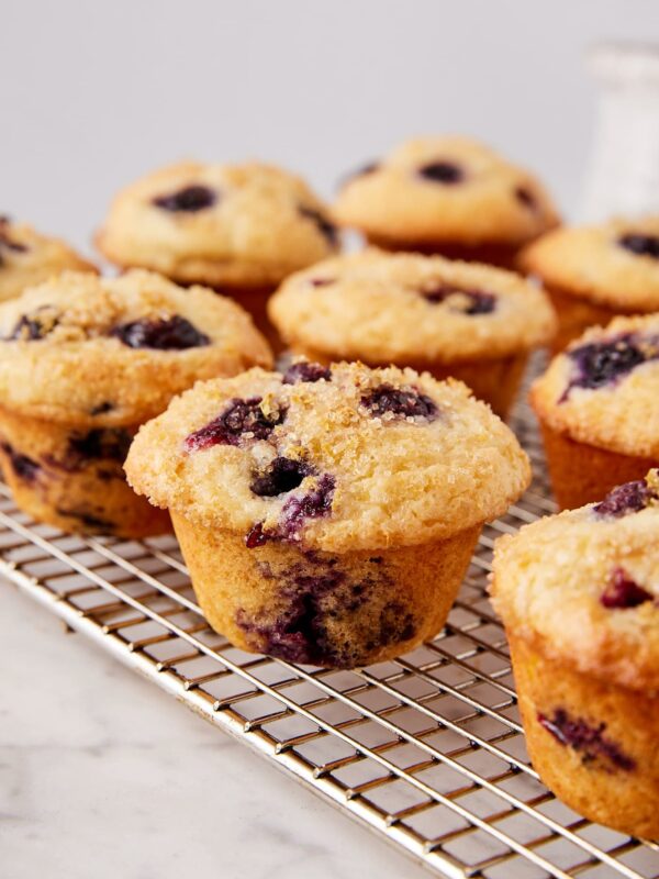 White marble surface with wire cooling rack with blueberry muffins cooling.