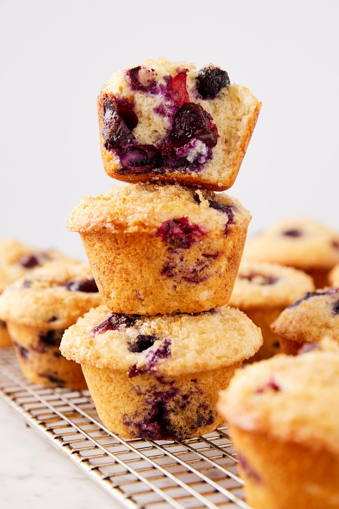 Three blueberry muffins stacked on top of each other with more muffins all around cooling after being baked.