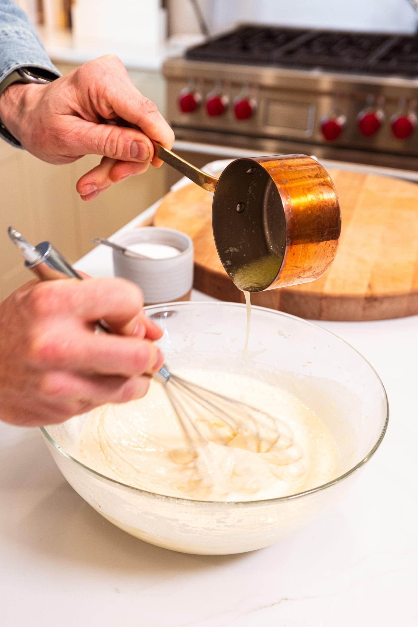 Hand holding small copper pot pouring melted butter into a batter for blueberry muffins.