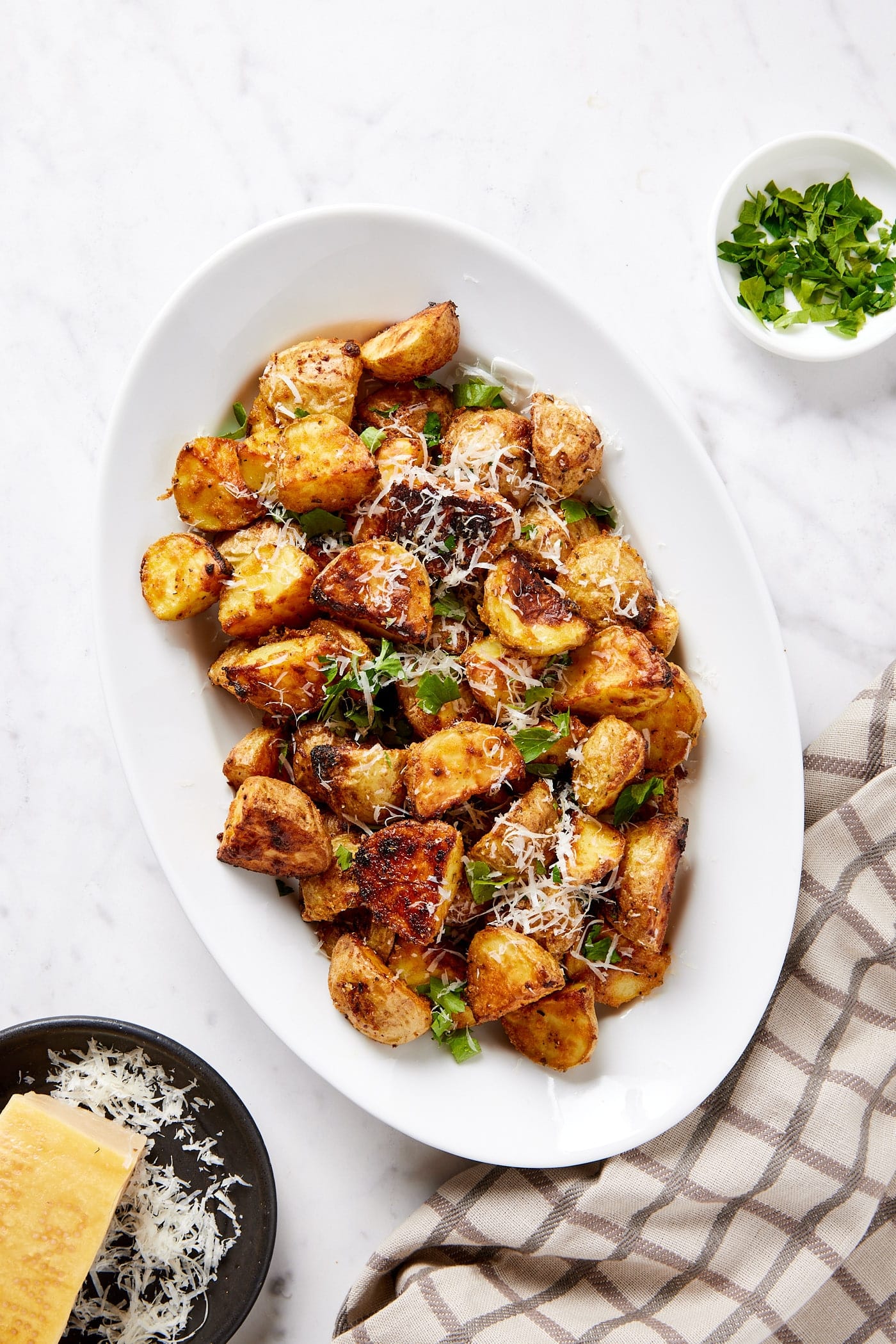 Oval dish filled with crispy rosemary roasted potatoes topped with fresh herbs and shredded cheese.