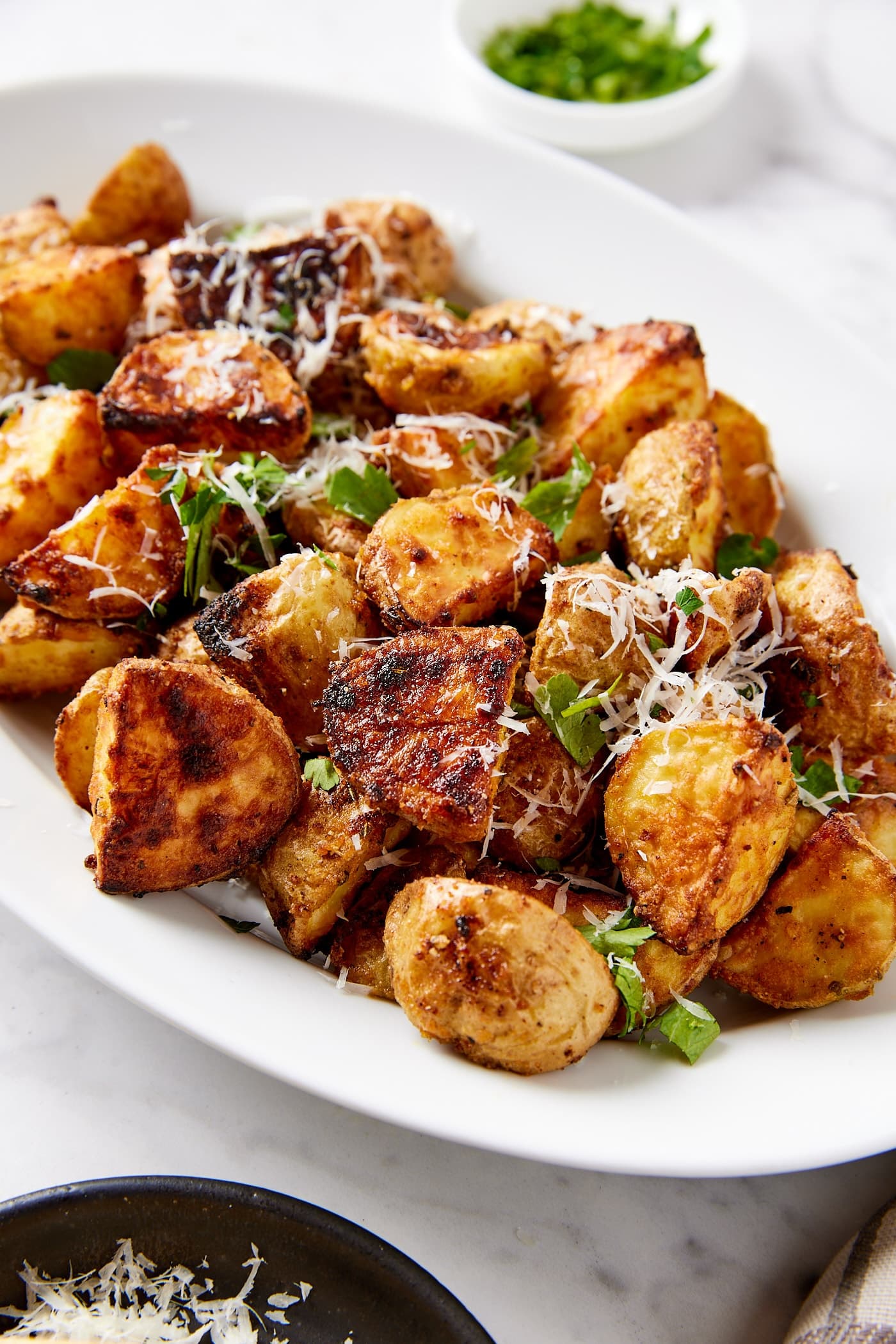 Oval serving platter filled with crispy rosemary roasted potatoes topped with chopped fresh herbs and shredded cheese.