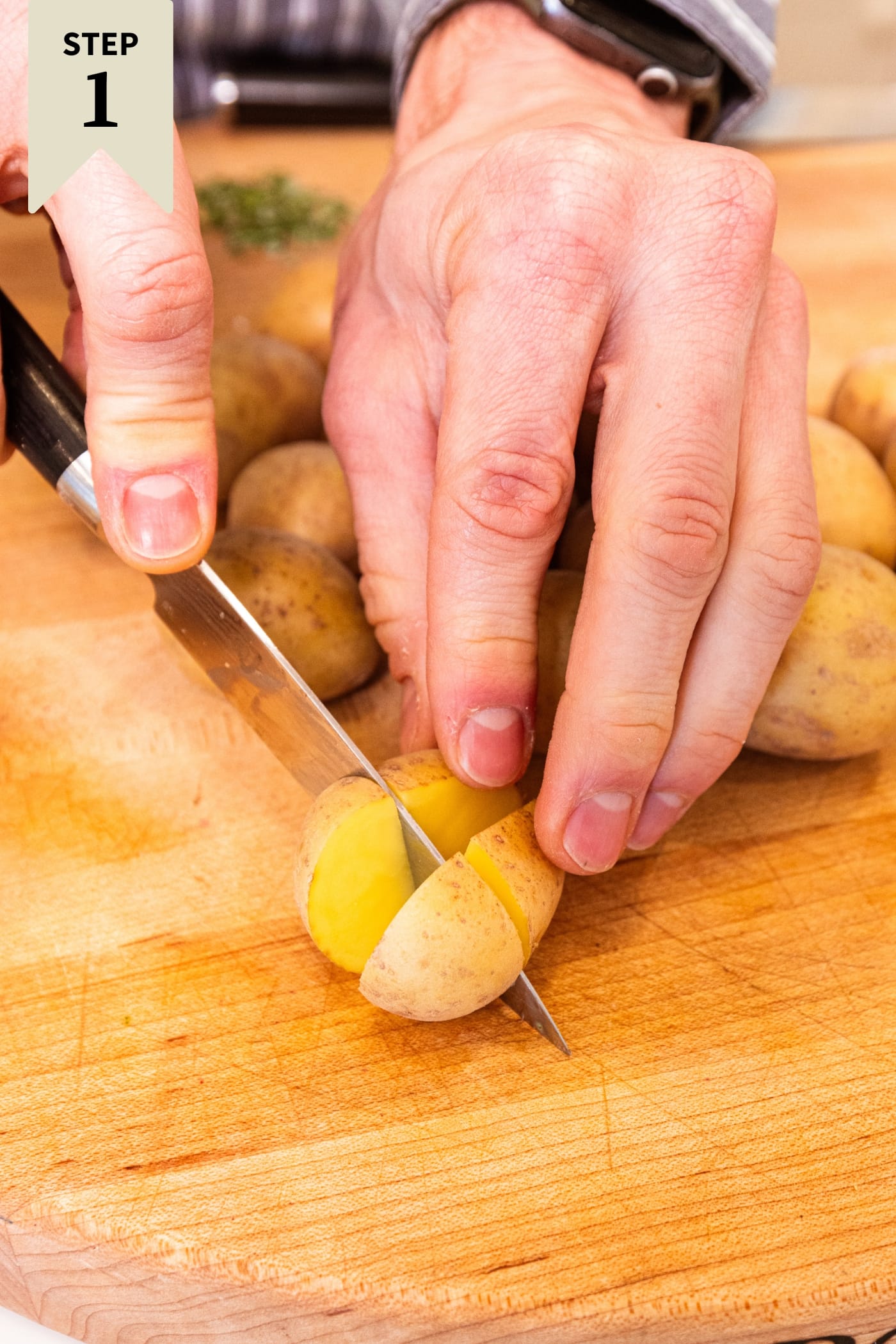 Hand slicing small potatoes into small quarters on a wooden cutting board.