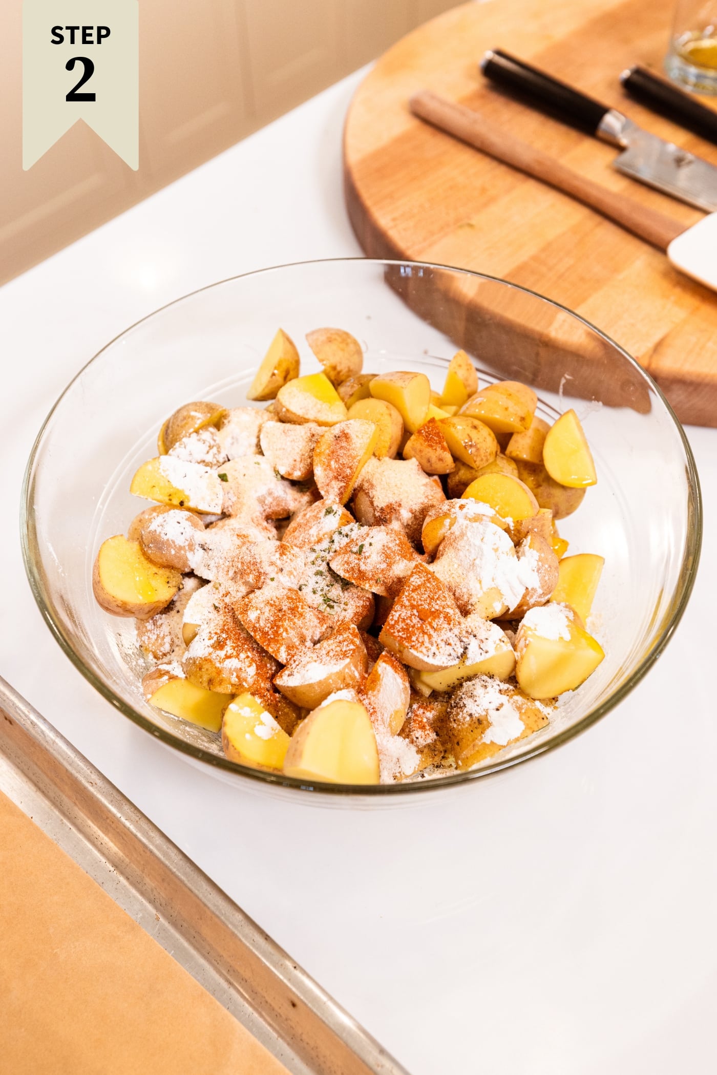 Glass bowl filled with sliced potatoes with spices dusted all over the top before being mixed together.