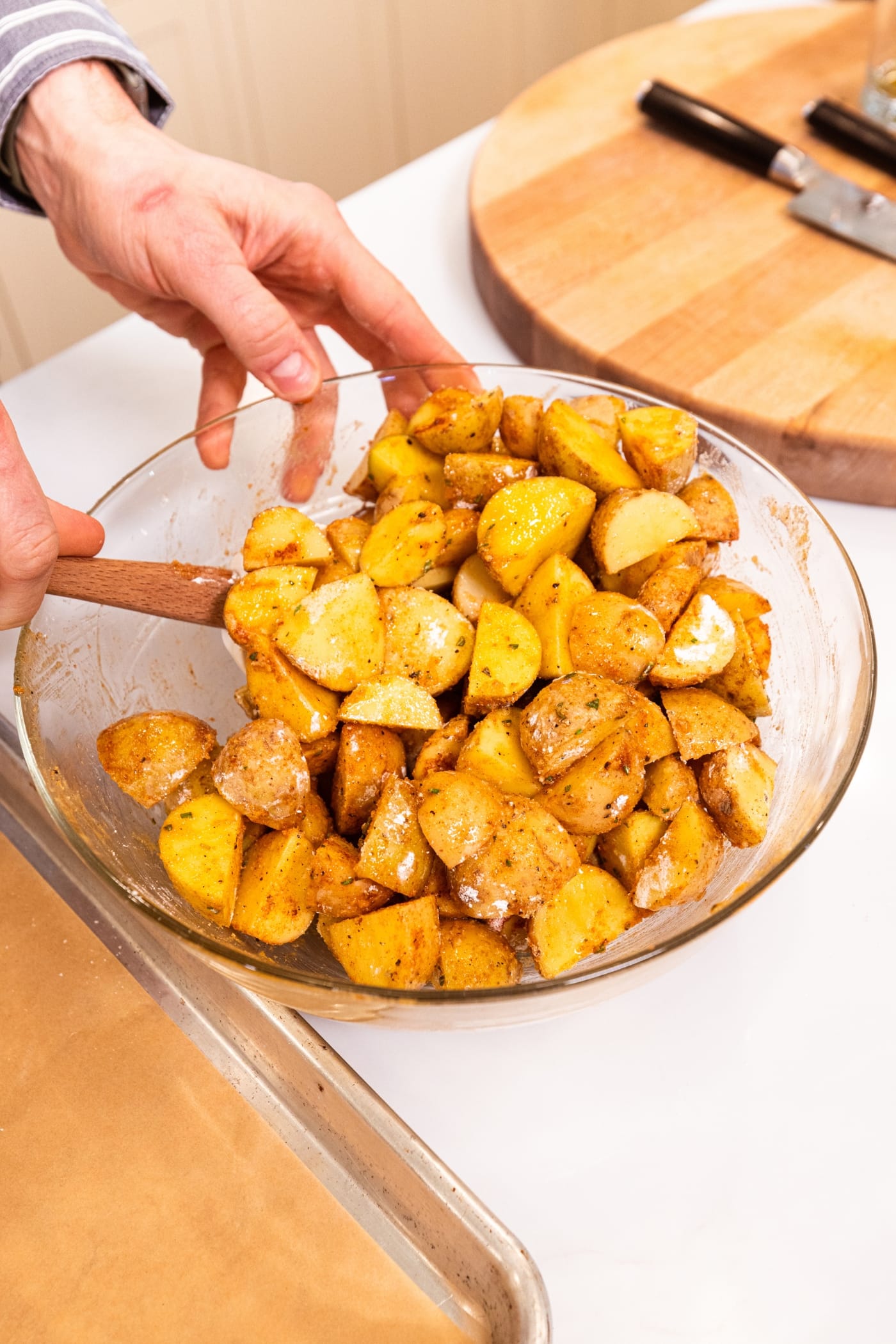 Hand using spatula mixing together blend of spices in glass bowl before baking.