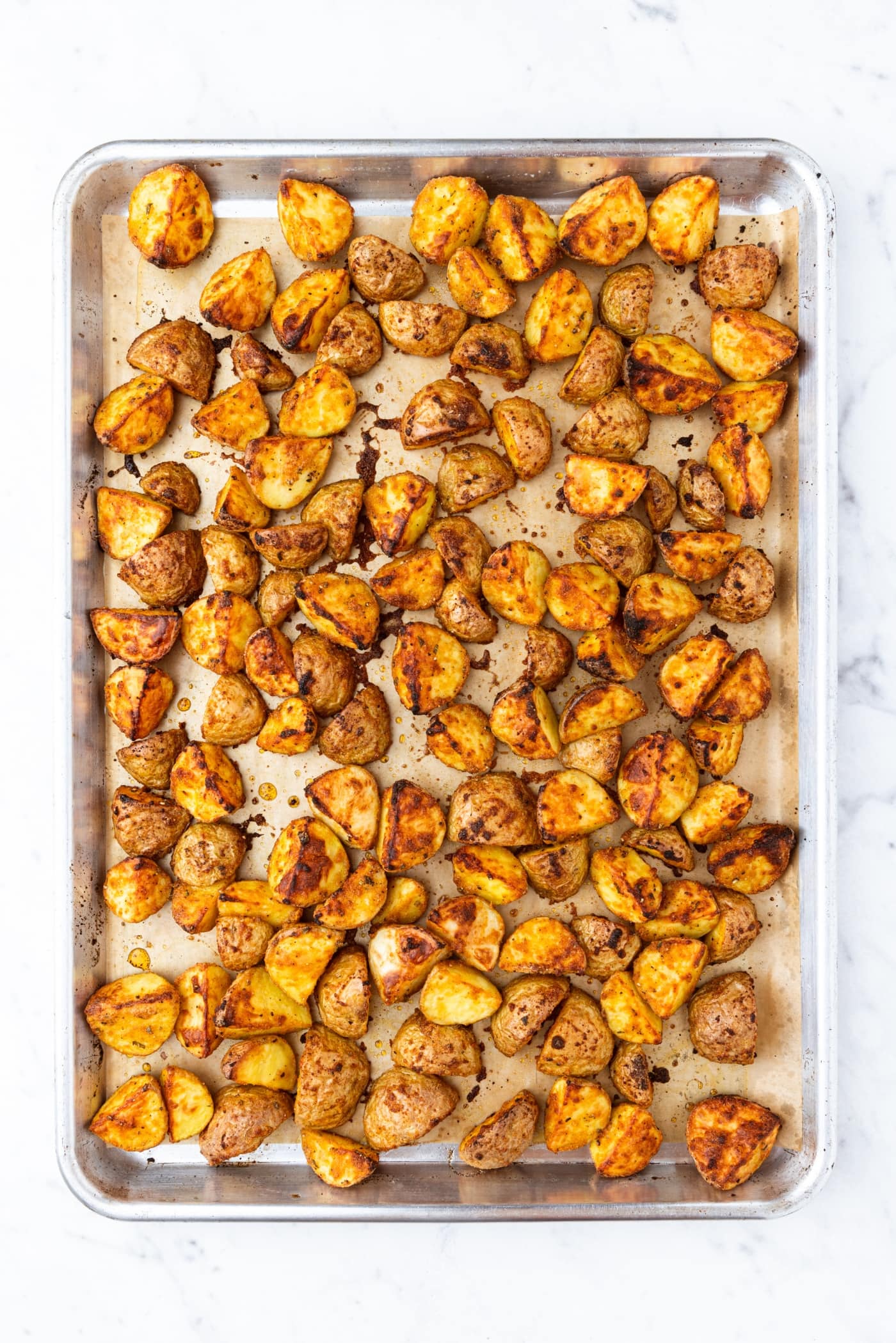 White marble surface with baking sheet with sliced roasted potatoes with spices all over the top.