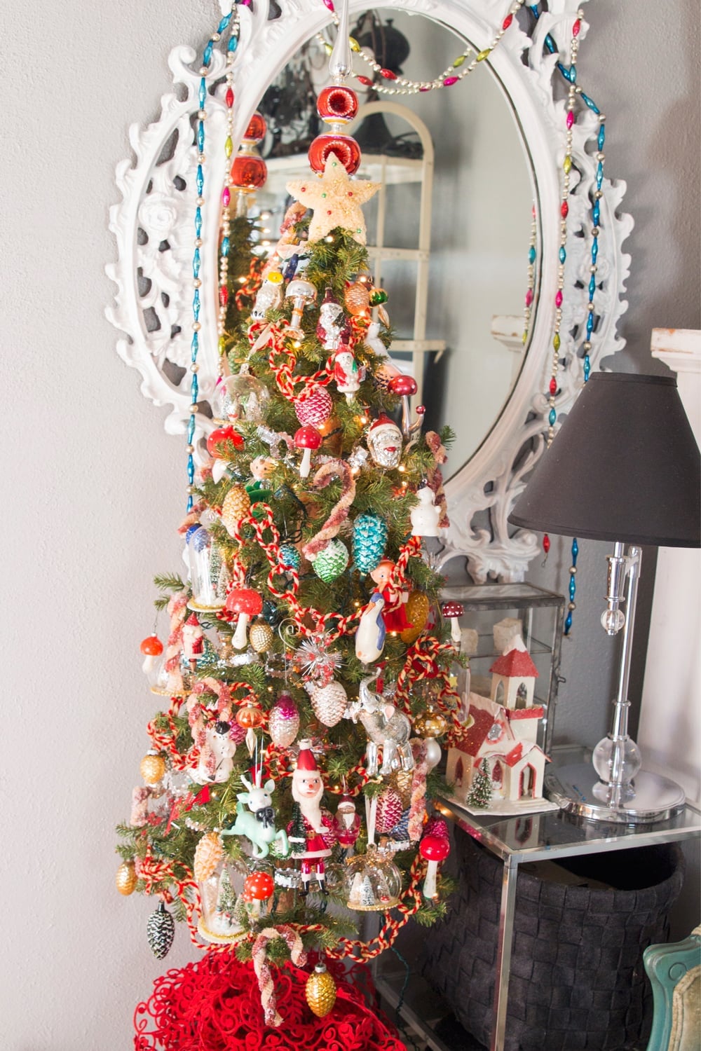 Tree with vintage ornaments in mostly colors of red with white oval mirror in the background.