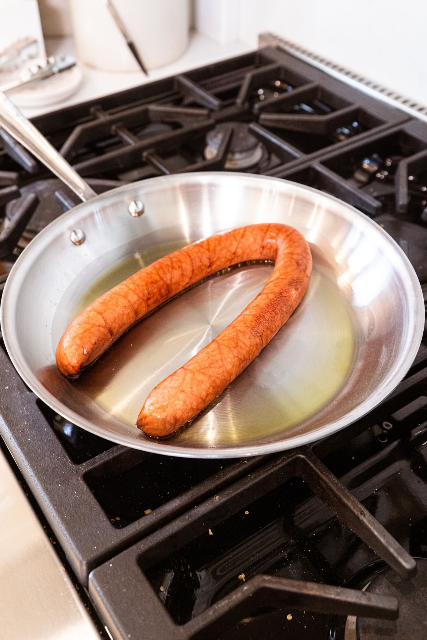 Kielbasa sitting in metal skillet with oil to begin browning the outer surface with a crust.