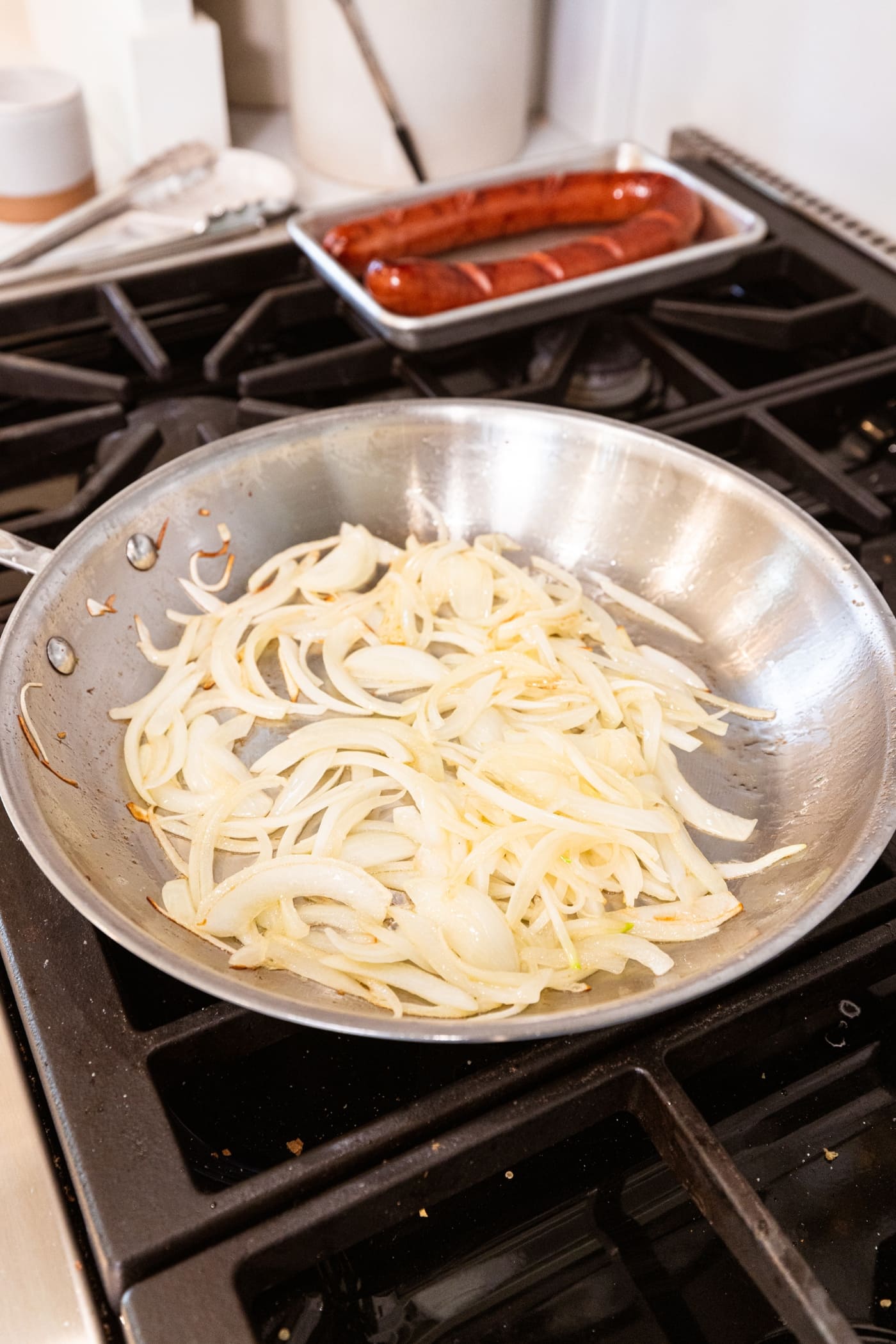 Slightly browned sliced onions in a metal skillet on the stovetop in oil.