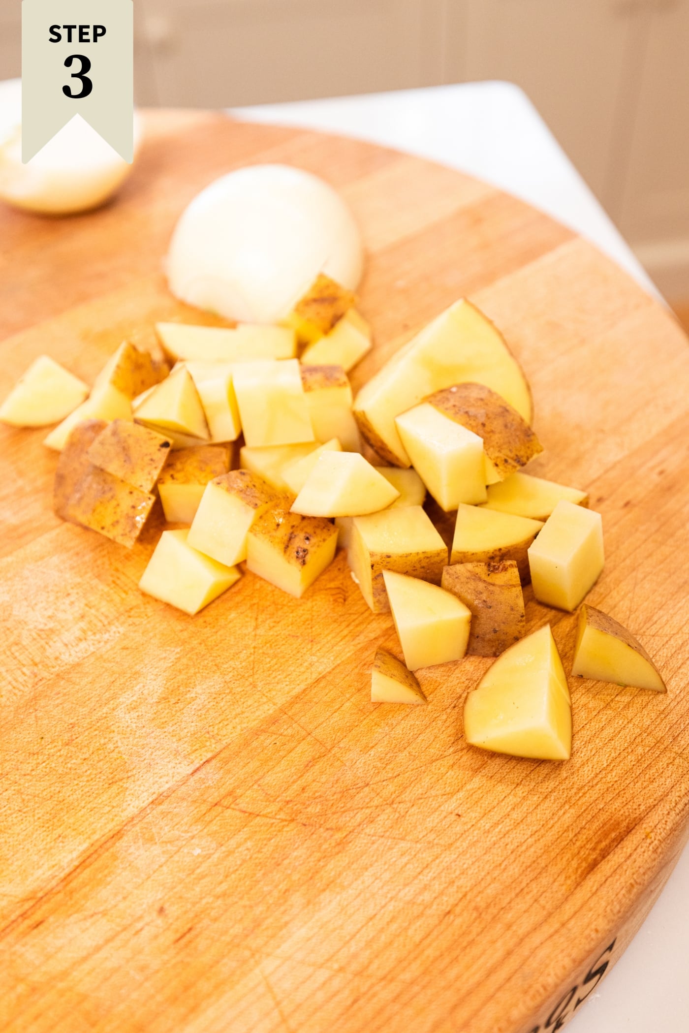 Diced gold potatoes sitting on wooden cutting board after being cut into pieces.