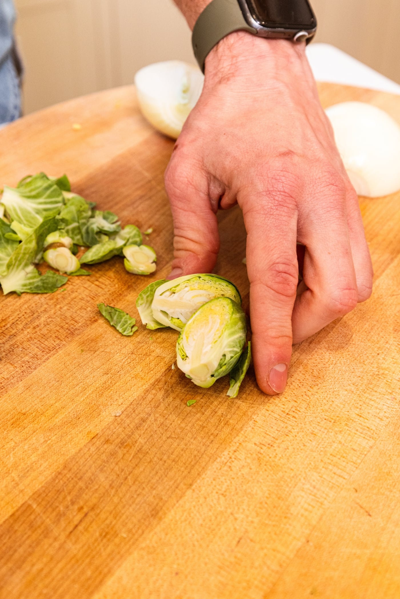 Brussels sprout being sliced in half showing the interior texture all on wooden cutting board.